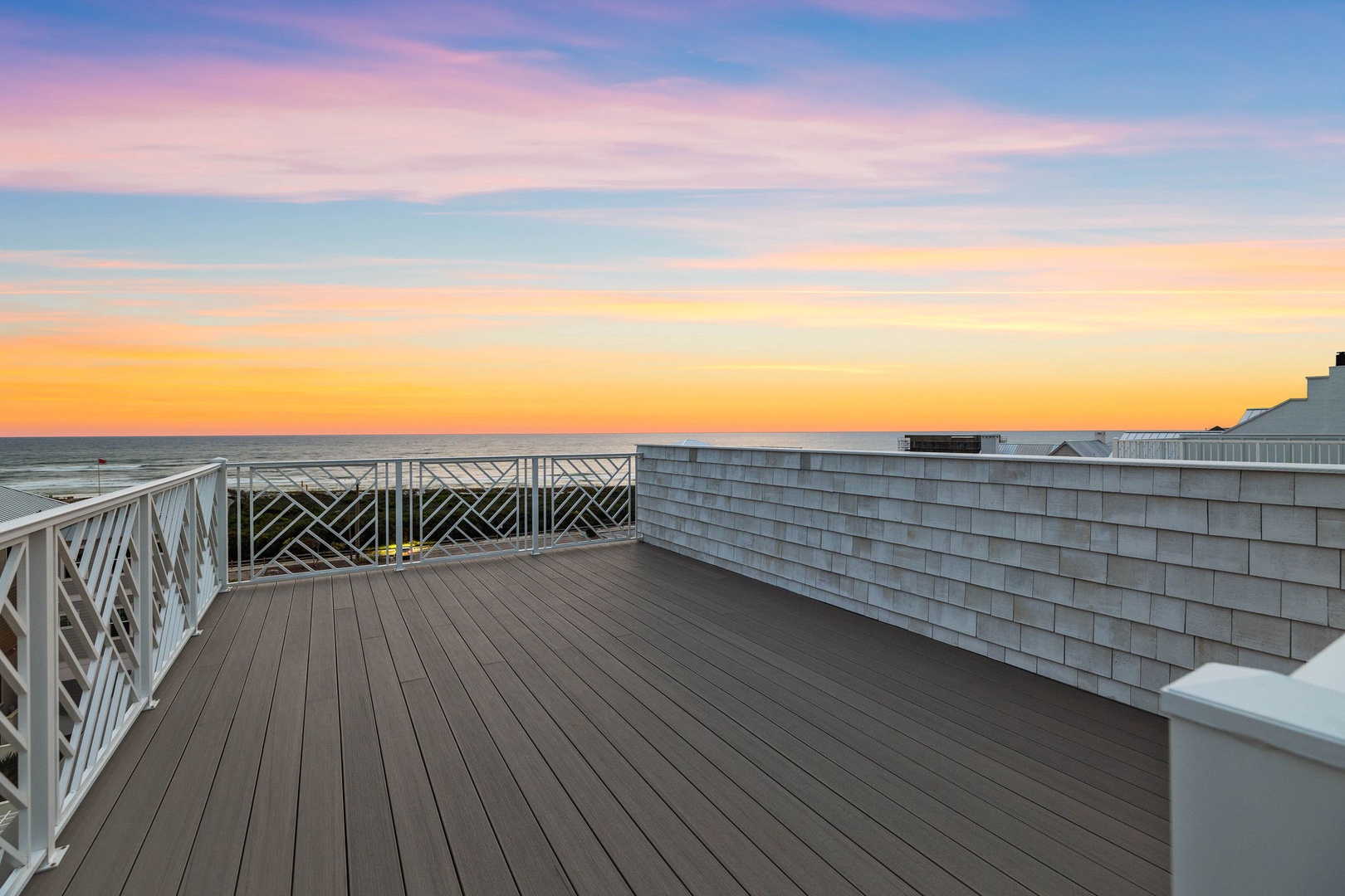 Breathtaking sunset sky paints vibrant colors over this oceanfront terrace with expansive decking and coastal views.