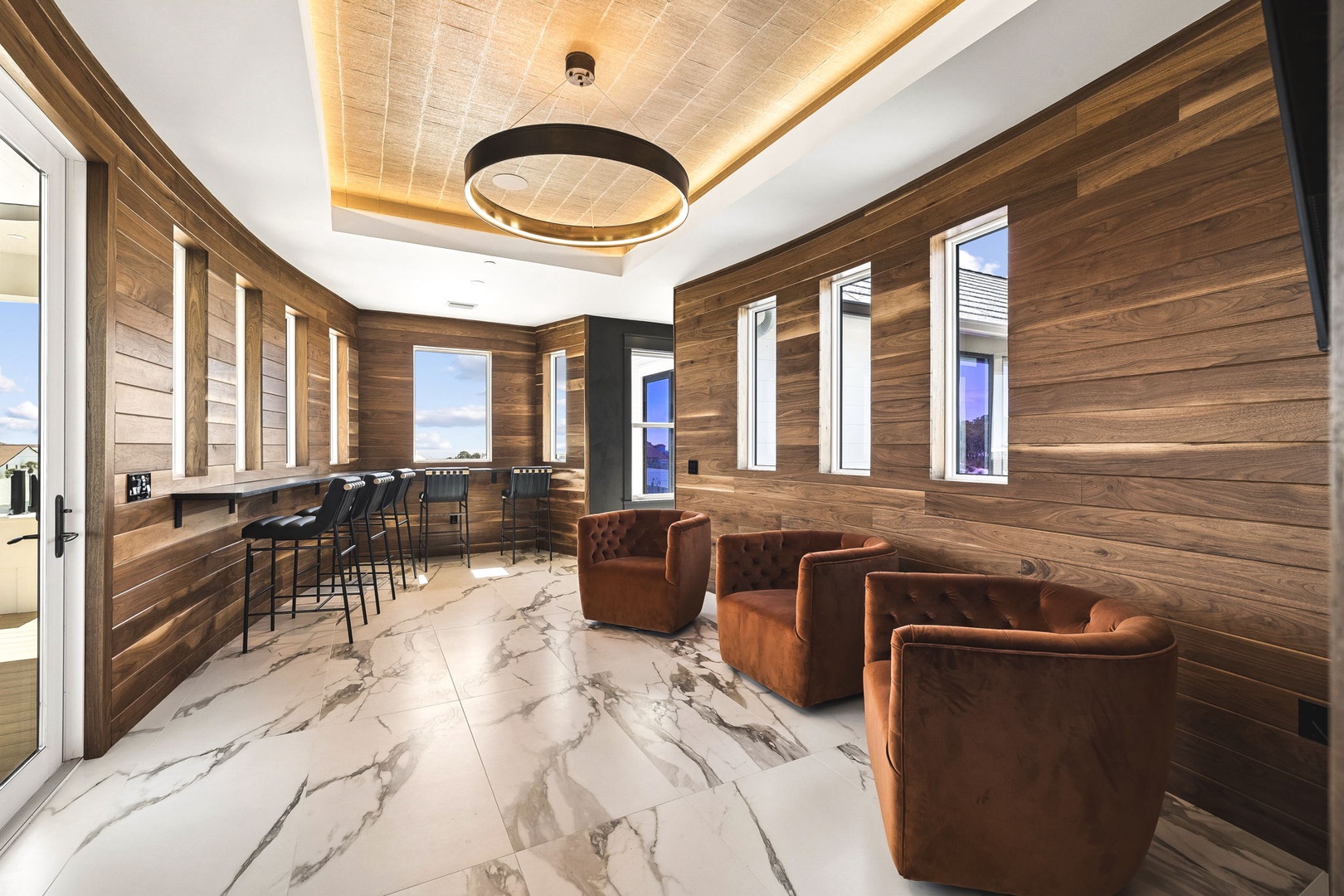 Settle into rich leather seating in this stunning wood-paneled lounge, where natural light streams through tall windows and a striking pendant casts a warm glow overhead—your perfect retreat for conversation or quiet reflection.