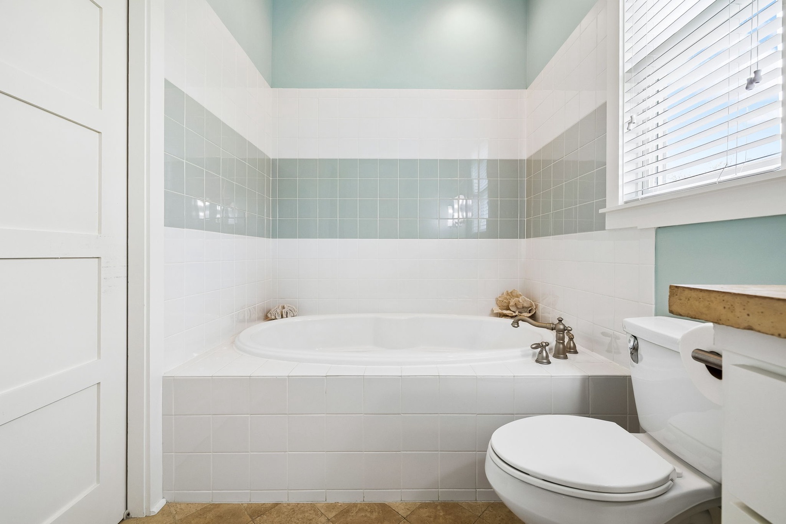 Relax in the bright coastal-inspired bathroom with soothing seafoam tile, a sunlit soaking tub, and coastal accents inviting you to unwind after your adventures.