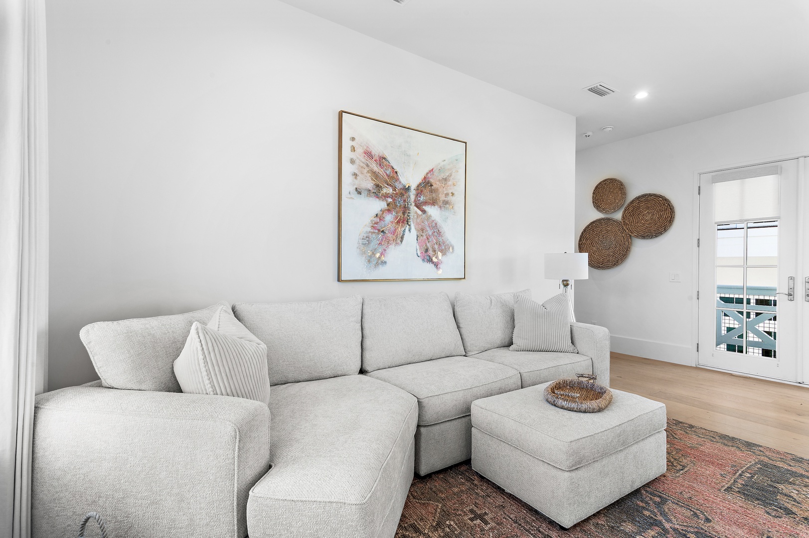 Relax on the plush sectional sofa while admiring charming artwork, woven wall accents, and abundant natural light streaming in from your private balcony access.