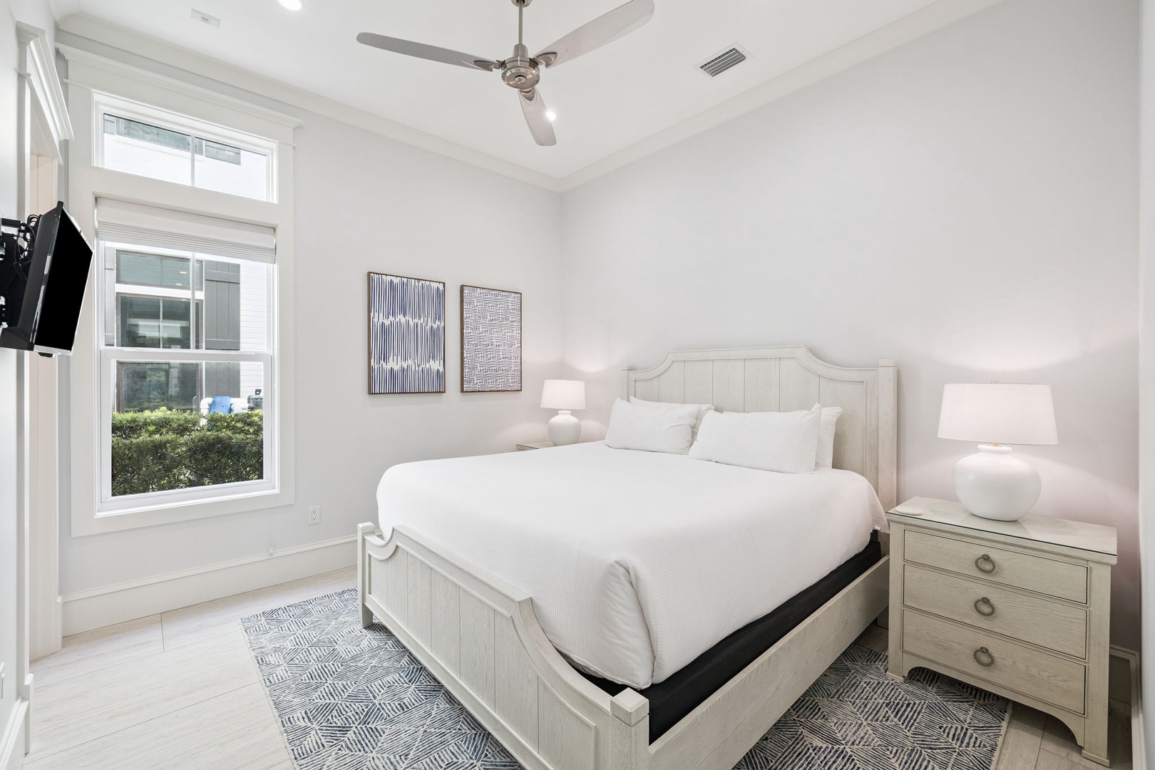 Drift off in your serene bedroom sanctuary, where crisp white linens meet modern comfort beneath a gentle ceiling fan.