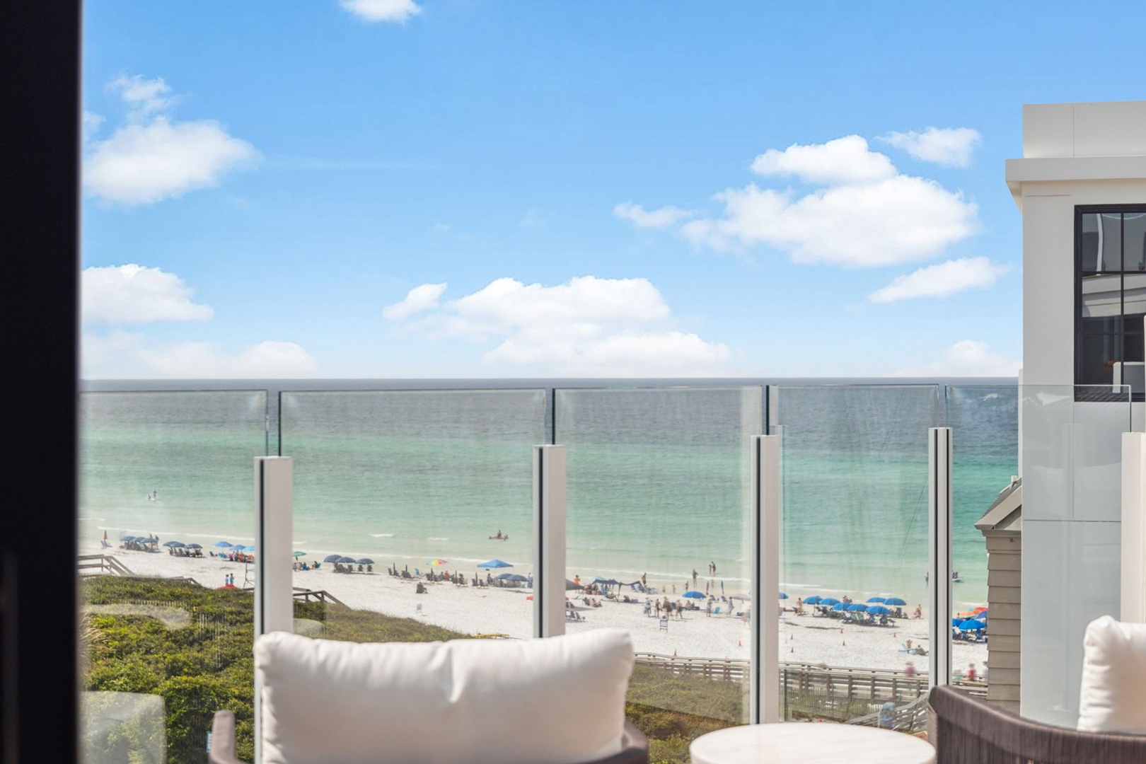 Stunning beachfront views stretch across turquoise waters and white sand, framed by a modern glass balcony. The perfect coastal retreat awaits just beyond your window.