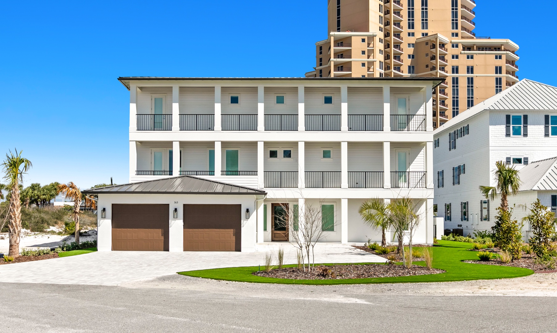 Modern three-story beachside residence featuring spacious balconies and coastal landscaping. The property sits in a quiet neighborhood with nearby high-rise towers and sandy beach access just steps away.
