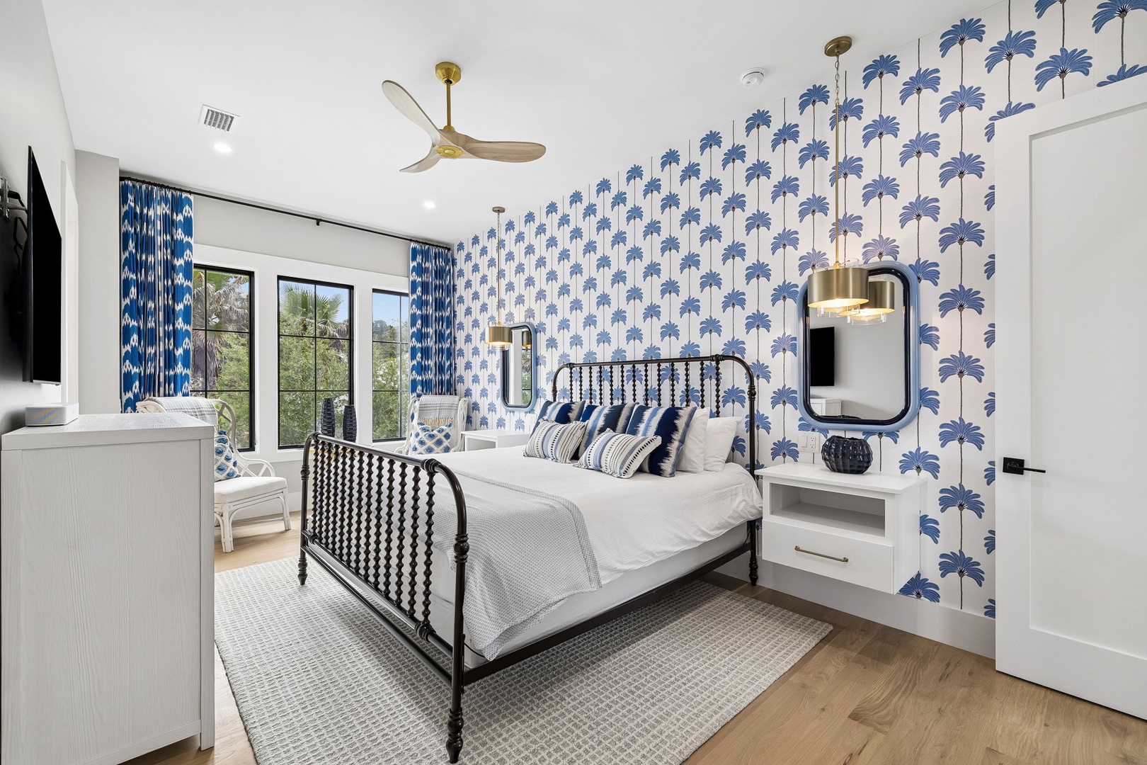 Your bright, airy bedroom features playful palm tree wallpaper, crisp white linens, and a cozy sitting area where you can unwind while enjoying serene garden views.