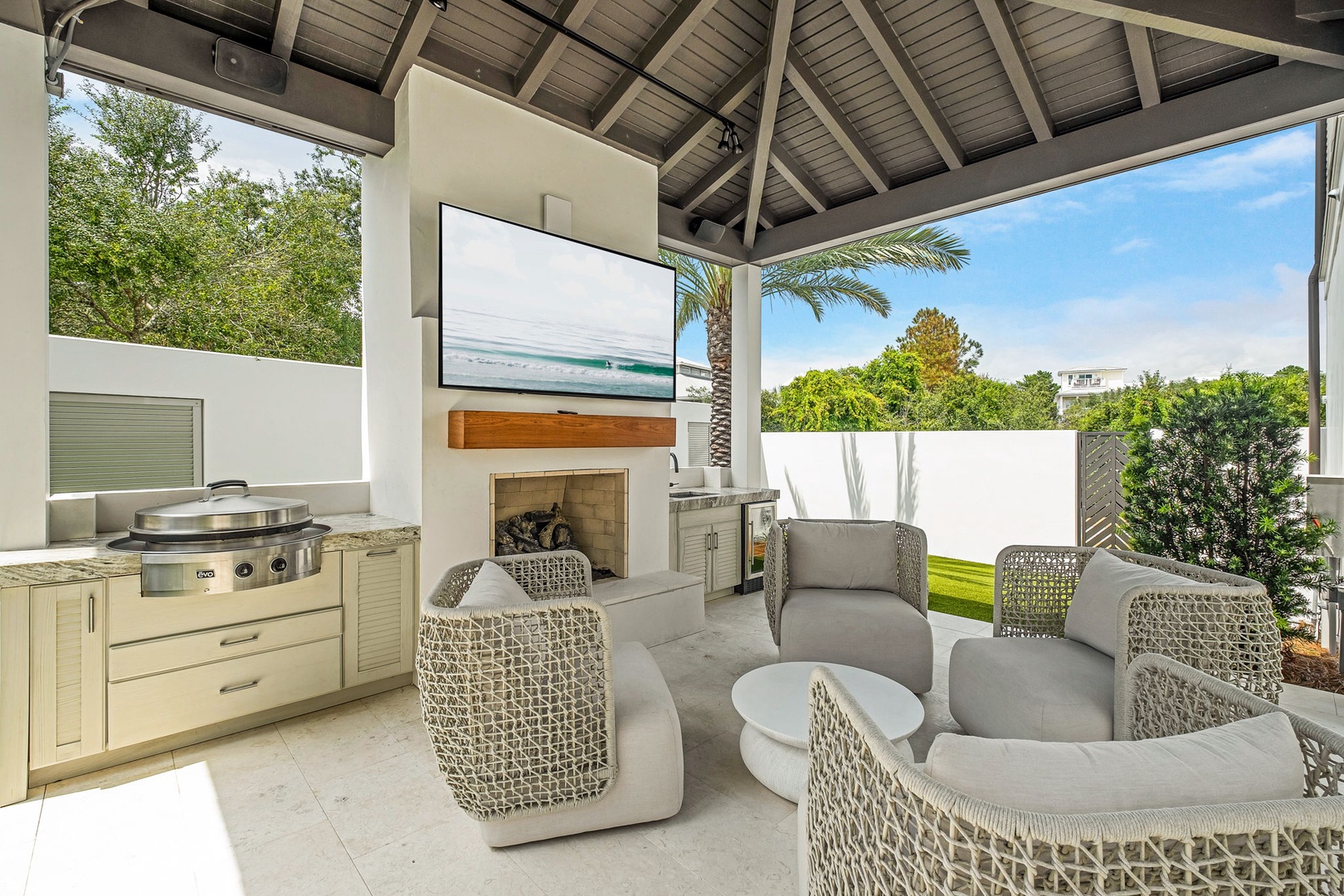 A stylish outdoor pavilion with a full kitchen, cozy fireplace, and plush seating invites you to unwind while enjoying lush garden views and open skies.