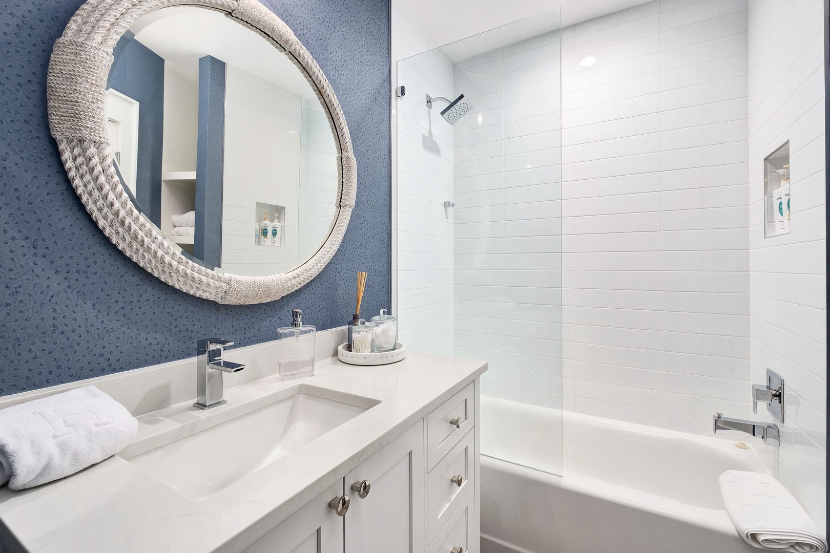Step into your bright bathroom with white tiled walls, a calming blue accent, and a stylish rope mirror. Unwind with a soak in the tub or a refreshing rinse.