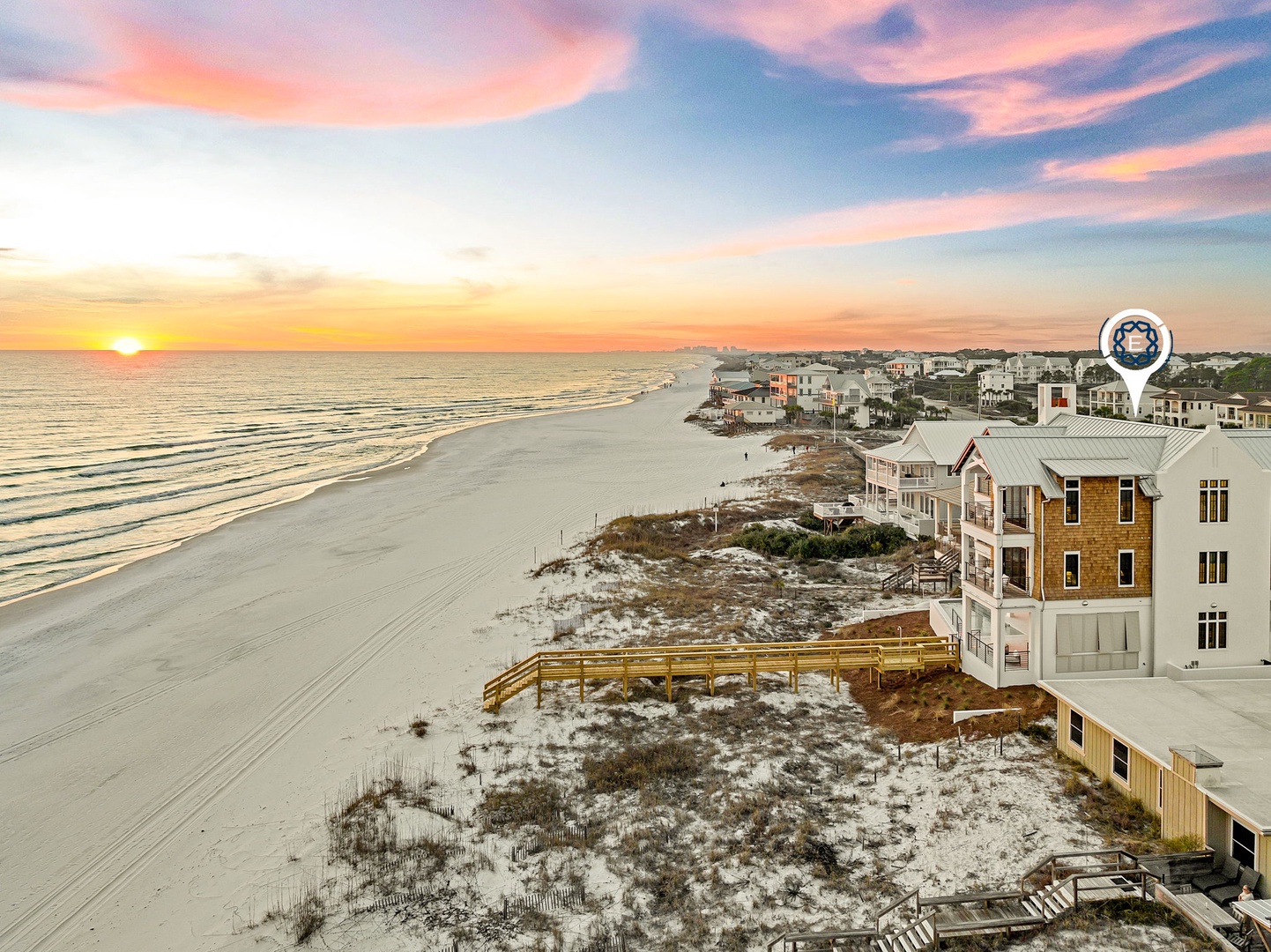 Stunning beachfront sunset paints the sky in brilliant oranges and pinks over pristine white sand and coastal homes.