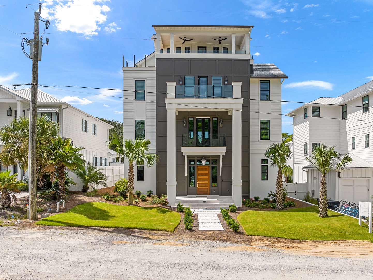 A modern coastal property with multiple balconies and palm-lined landscaping, situated in a quiet residential neighborhood just moments from the beach.