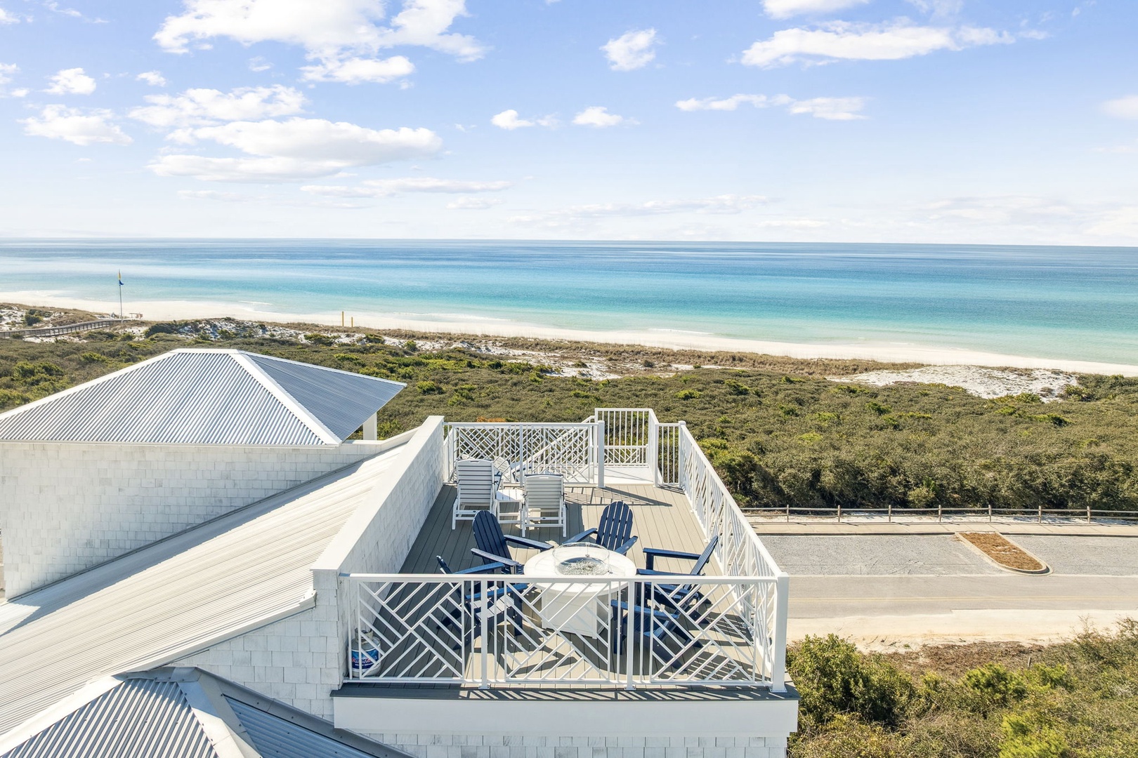 Elevated rooftop deck with stunning ocean views, featuring blue chairs and white railings overlooking pristine beach and coastline.