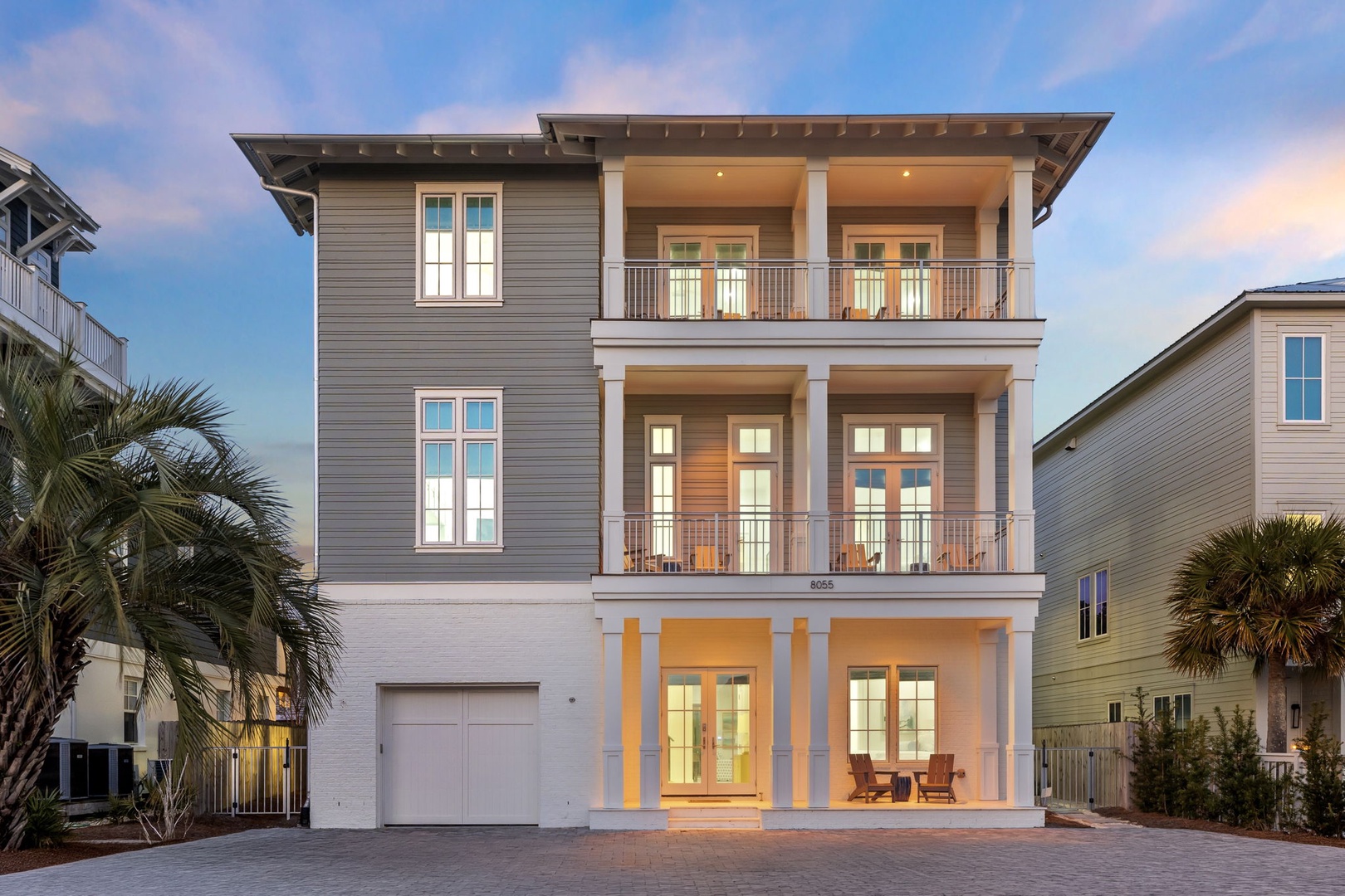 Beautiful three-story coastal home with spacious balconies and palm trees in a charming beachside neighborhood.