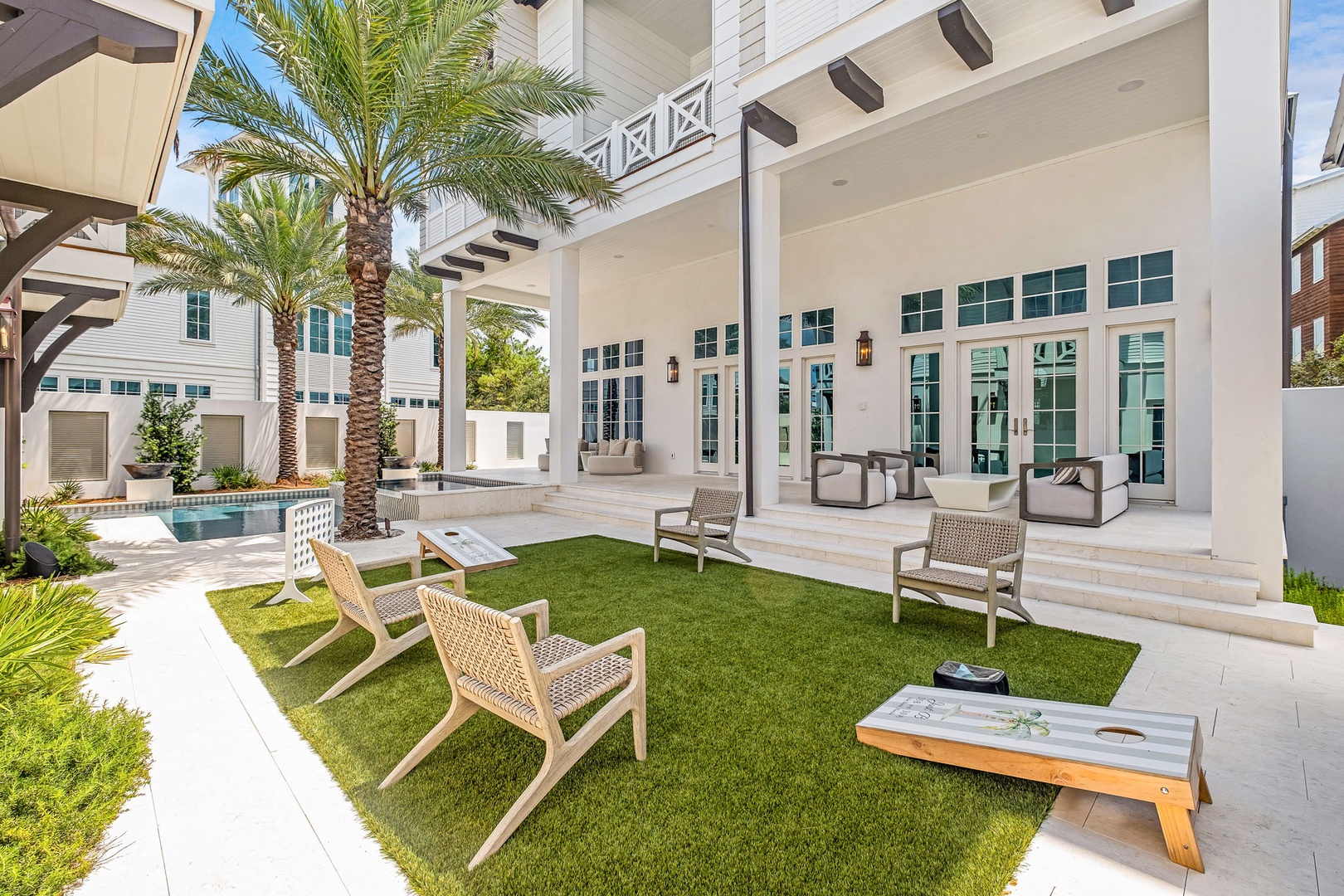 A sophisticated coastal retreat features a private courtyard with manicured lawn, intimate seating areas, and swaying palms, all anchored by a covered patio that seamlessly connects indoor and outdoor living.