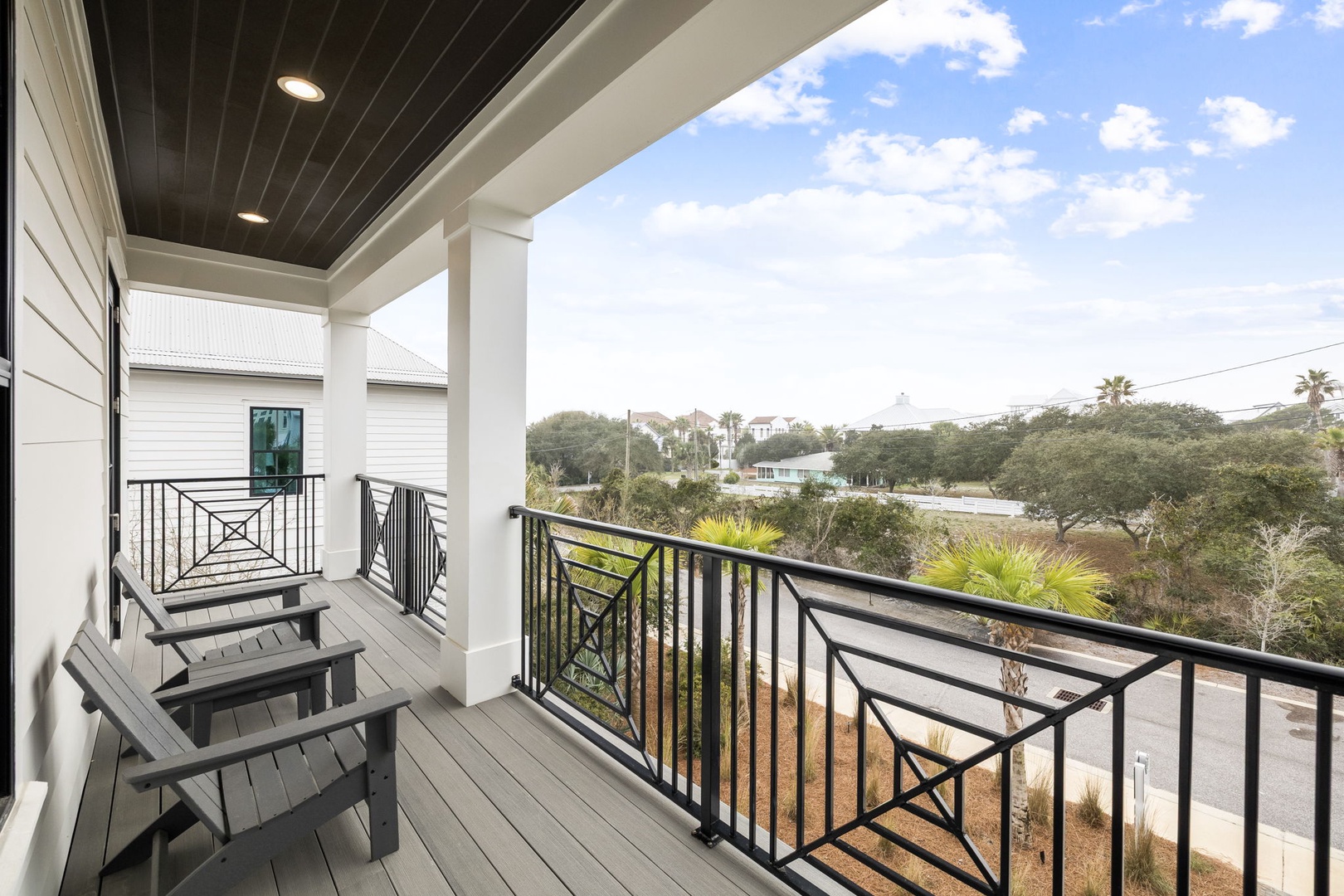 Covered balcony with comfortable seating overlooking a scenic neighborhood landscape with palm trees and natural vegetation.