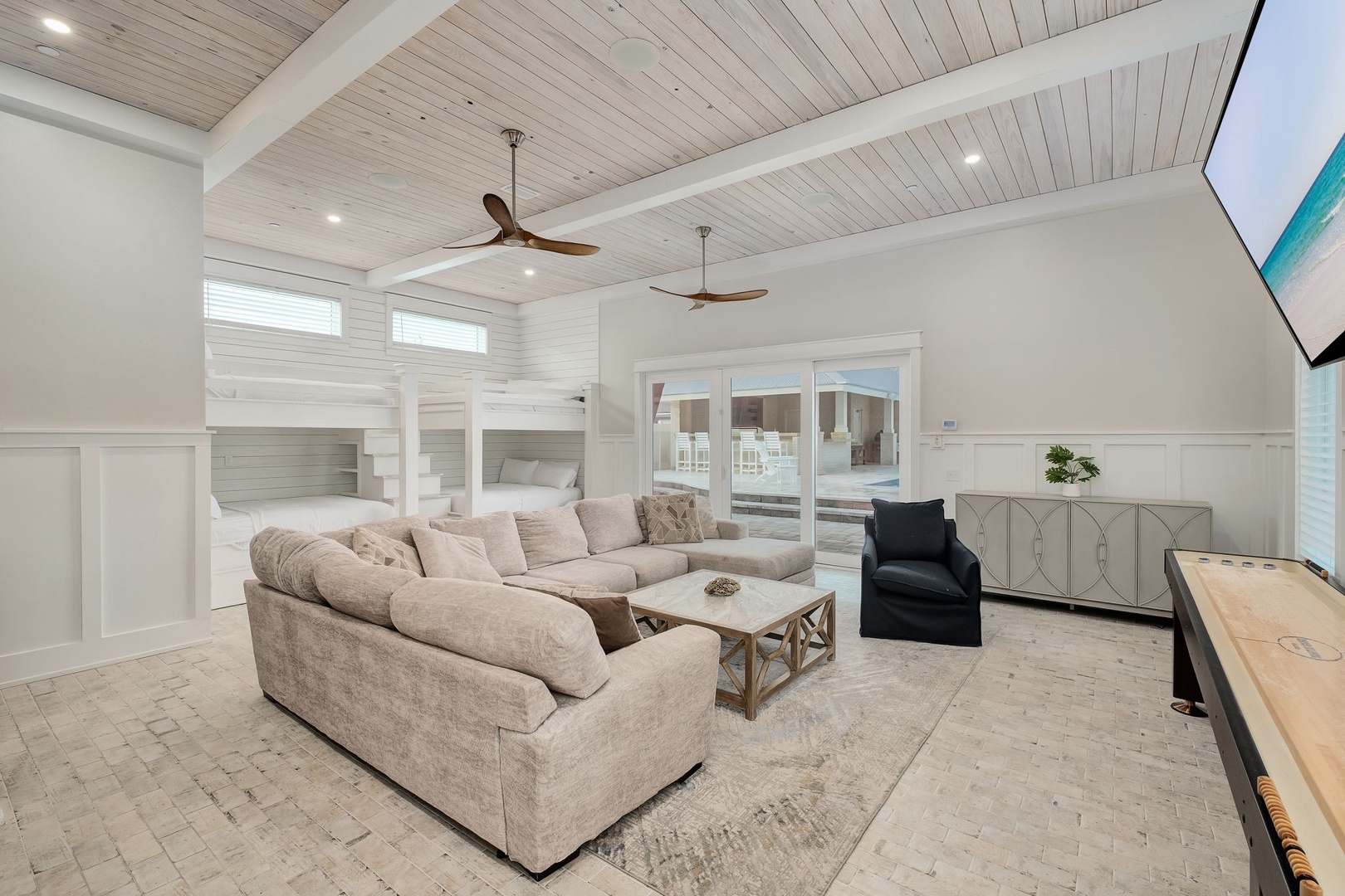 Unwind in your spacious living room featuring soaring wood-beam ceilings, plush sectional seating, and warm coastal elegance that makes every moment feel like home.