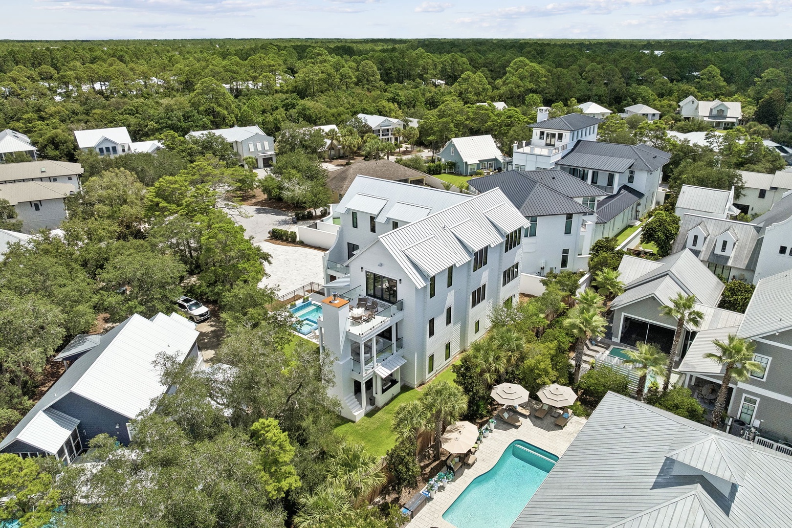 Aerial view of the property nestled within a lush, tree-lined coastal neighborhood, showcasing its prominent architecture and private pool area.
