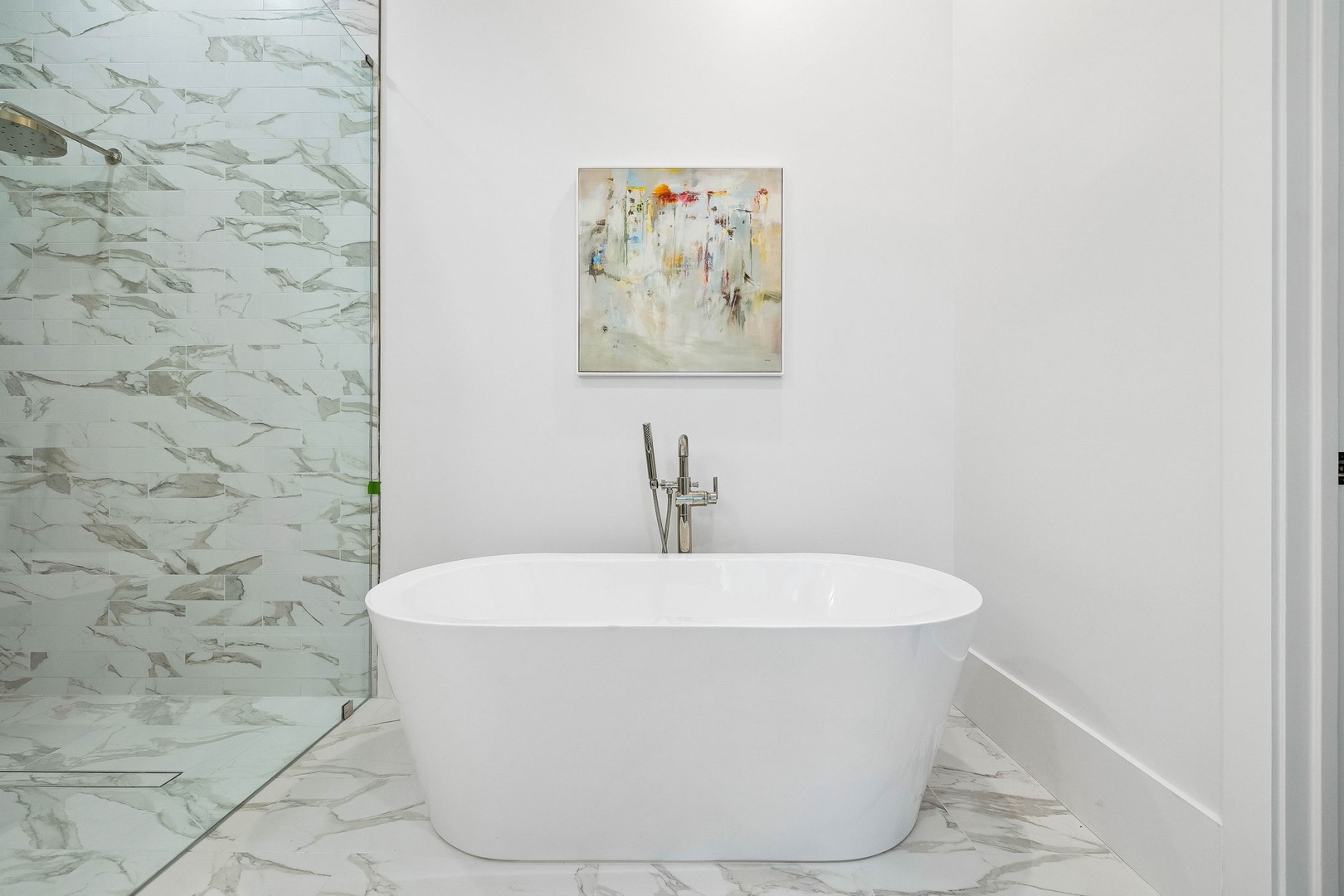 Sink into pure relaxation in your modern freestanding tub surrounded by elegant marble surfaces and a stunning glass-enclosed shower with artistic tilework.