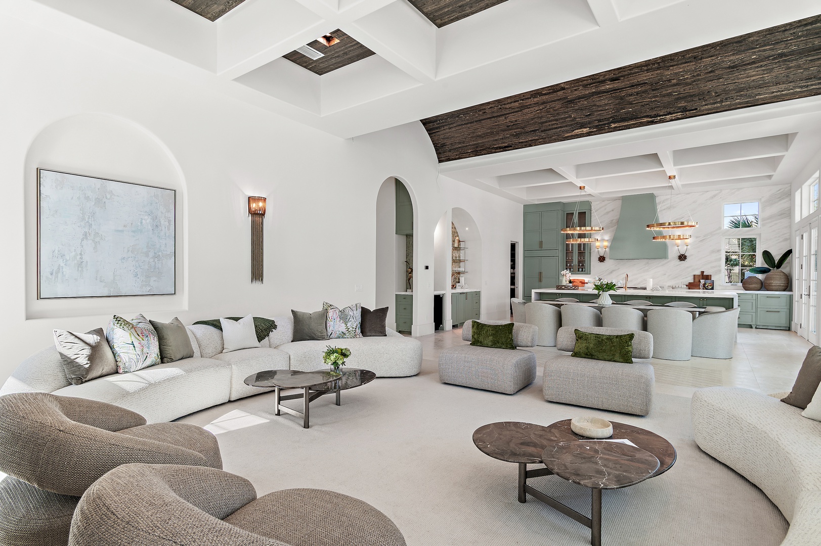 Unwind in this elegant open-concept living room, where natural light pours through arched doorways and a coffered ceiling with rustic wood beams frames your view into a stylish kitchen perfect for gathering.