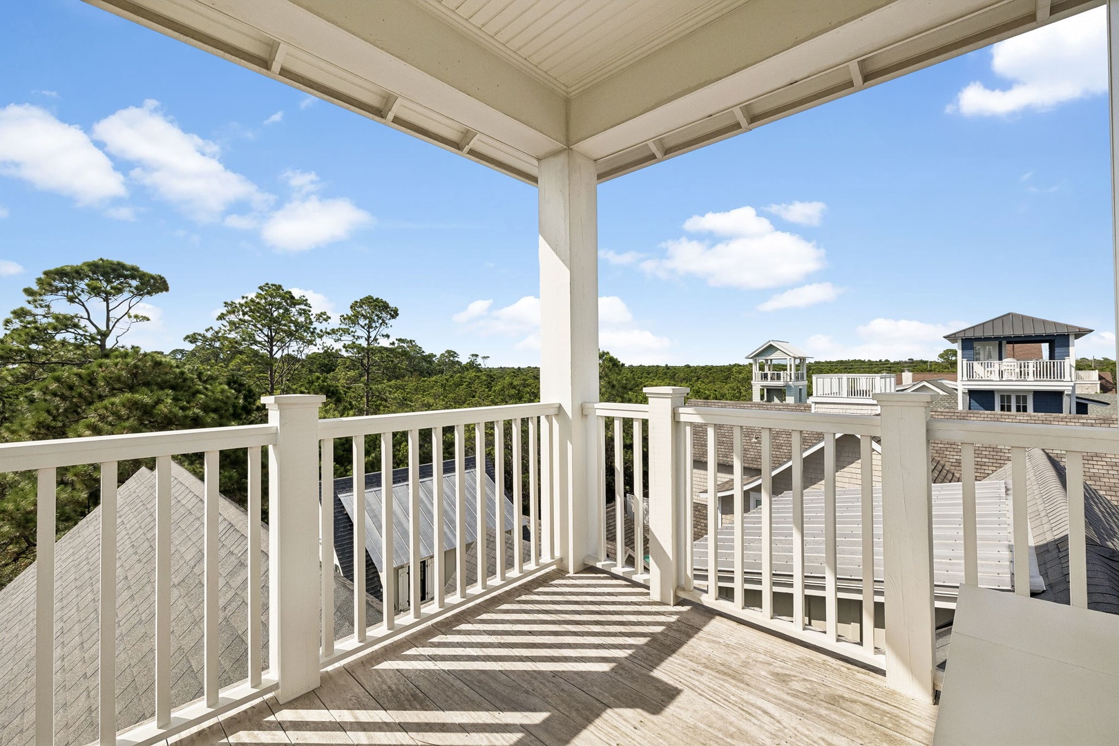 A covered balcony overlooking a peaceful residential neighborhood surrounded by mature trees under bright skies—ideal for morning coffee or unwinding at day's end.