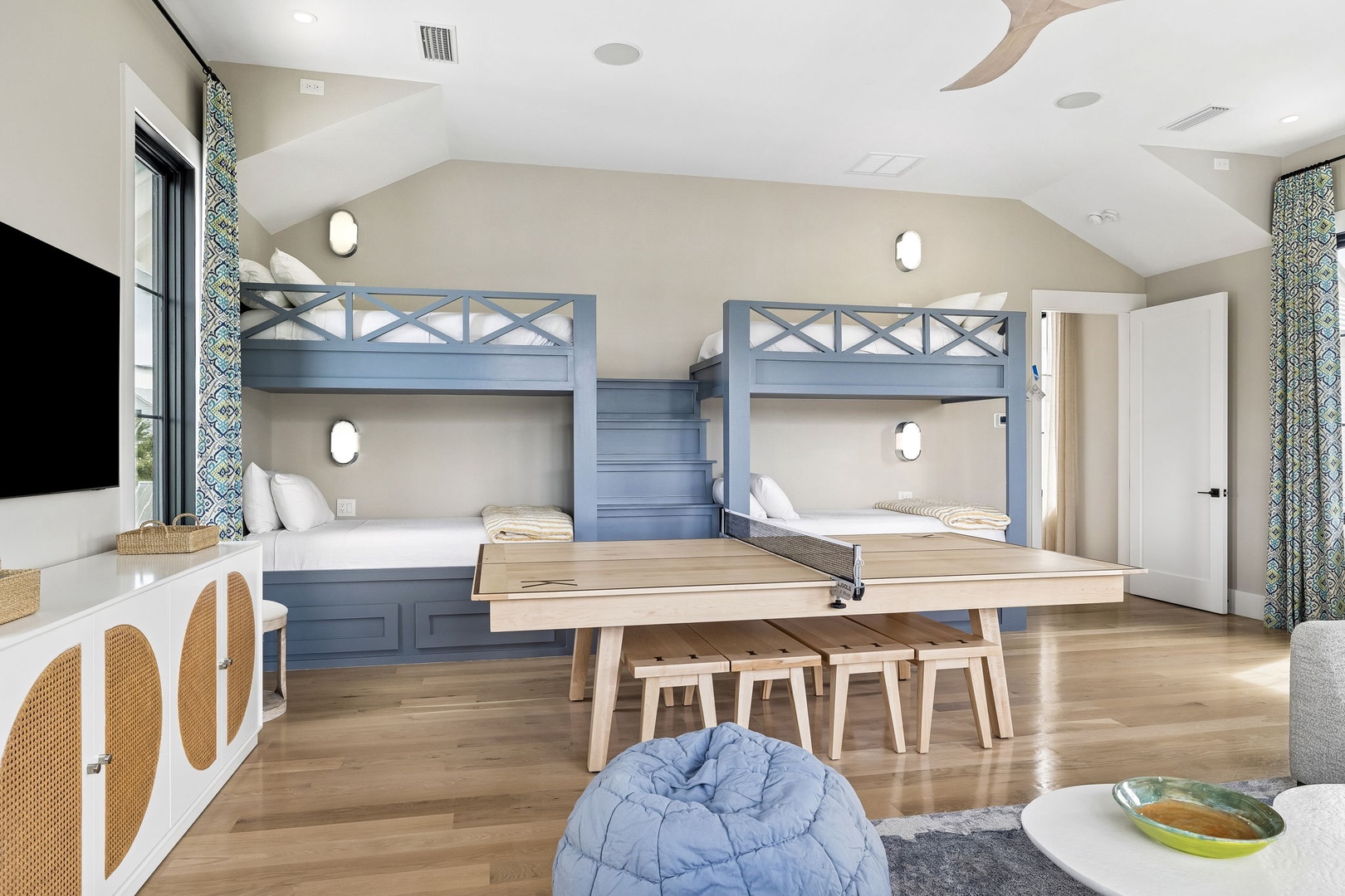 Gather the family in this spacious bunk room where custom-built beds and a play table create memories. Coastal-chic design meets comfort with vaulted ceilings and warm wood floors.