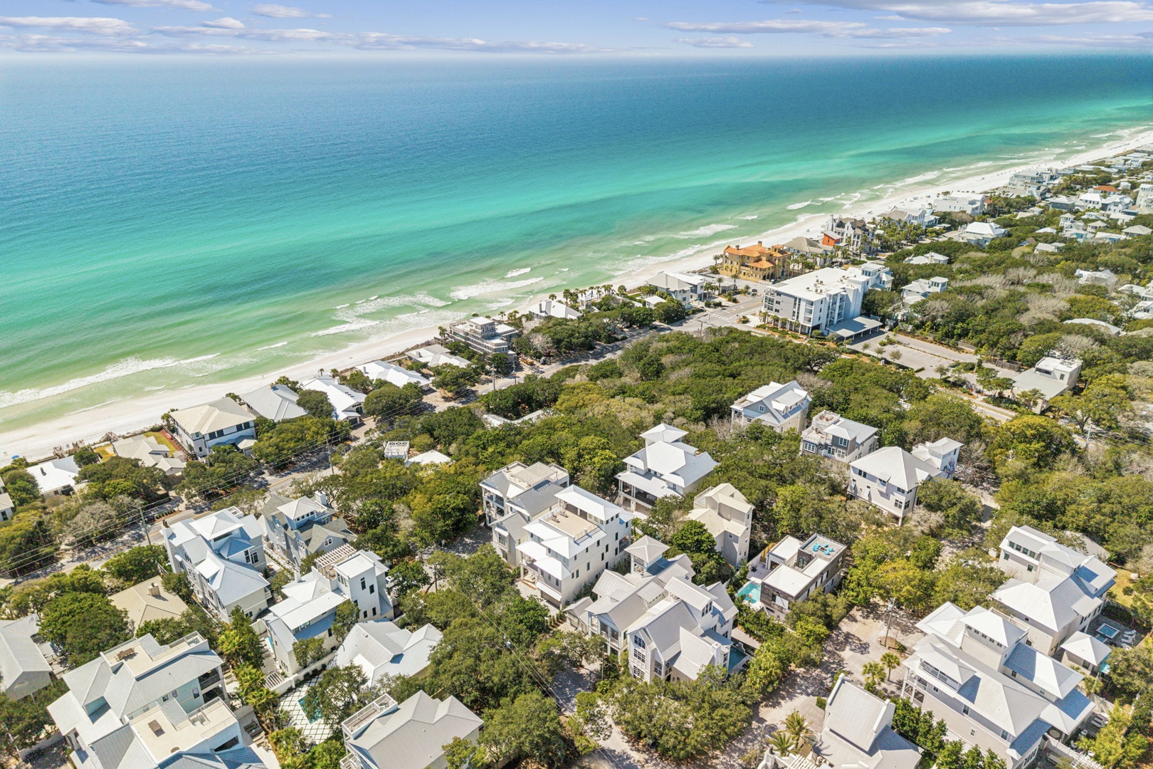 Stunning aerial view showcases this coastal community nestled between emerald Gulf waters and lush vegetation, just steps from pristine white sand beaches.