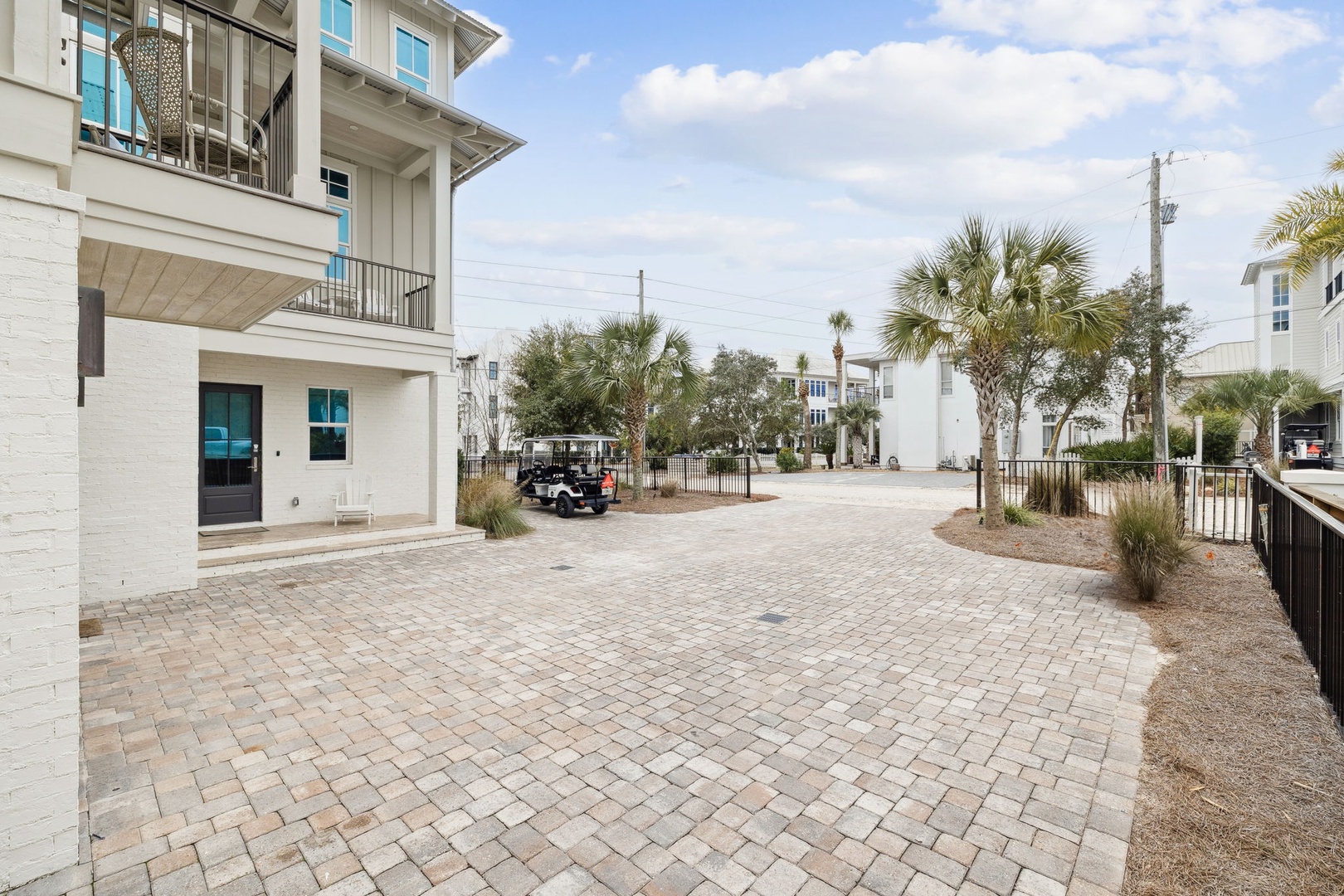 Spacious paved courtyard area featuring tropical palm trees and modern coastal architecture in a residential setting.