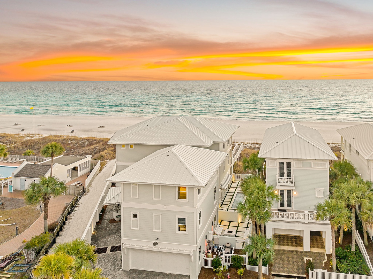 Stunning beachfront property nestled along pristine white sand, with colorful sunset skies painting the horizon. Palm trees frame the coastal architecture, offering direct beach access and tranquil ocean views.
