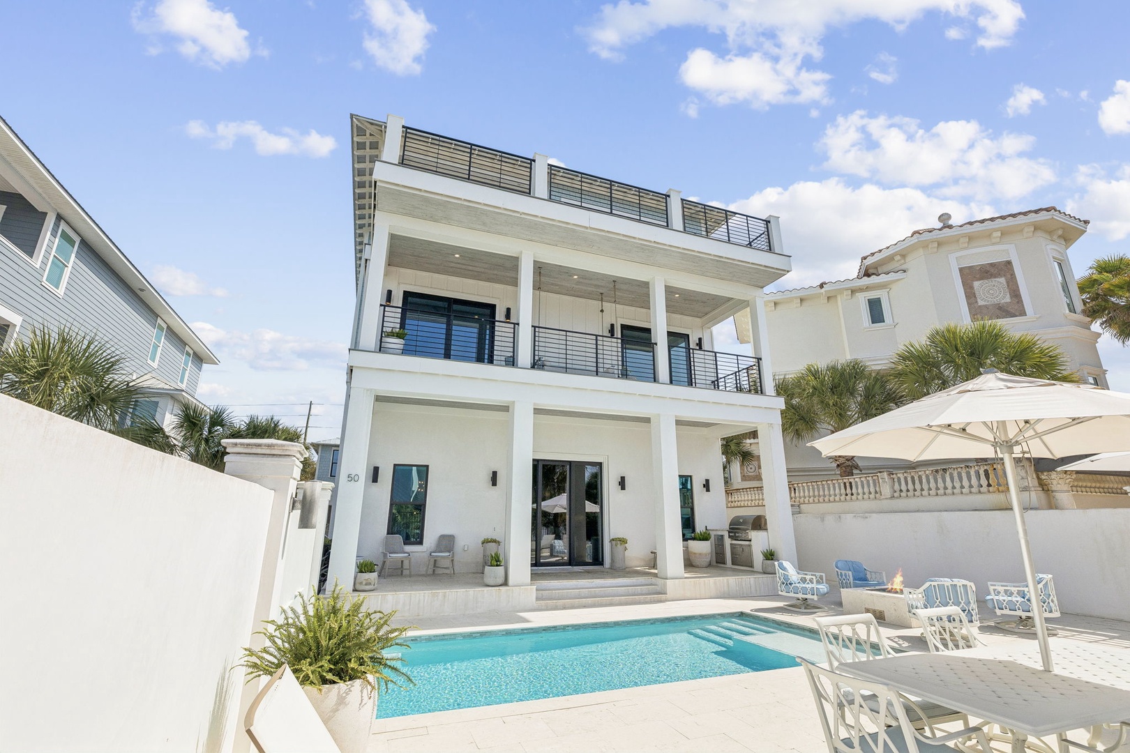 Modern three-story beach house featuring a sparkling pool, rooftop deck, and tropical surroundings in an upscale coastal neighborhood.