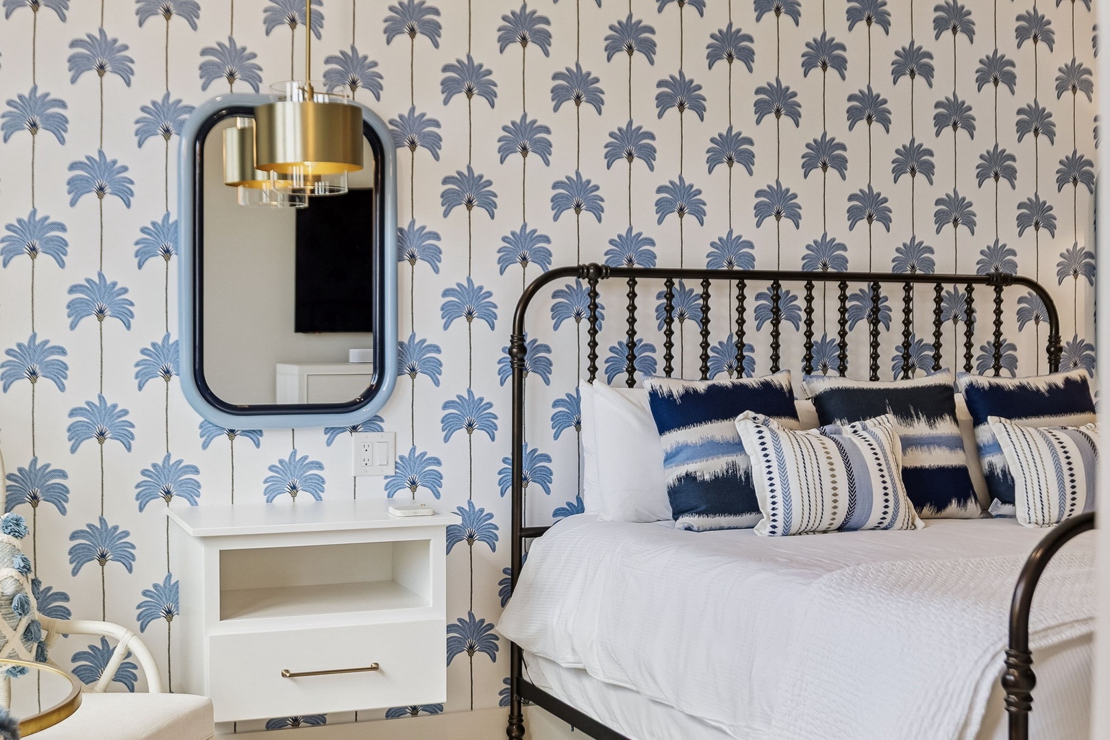 Sink into plush bedding beneath a stylish brass pendant while blue palm tree wallpaper adds a coastal, relaxed vibe to your retreat.