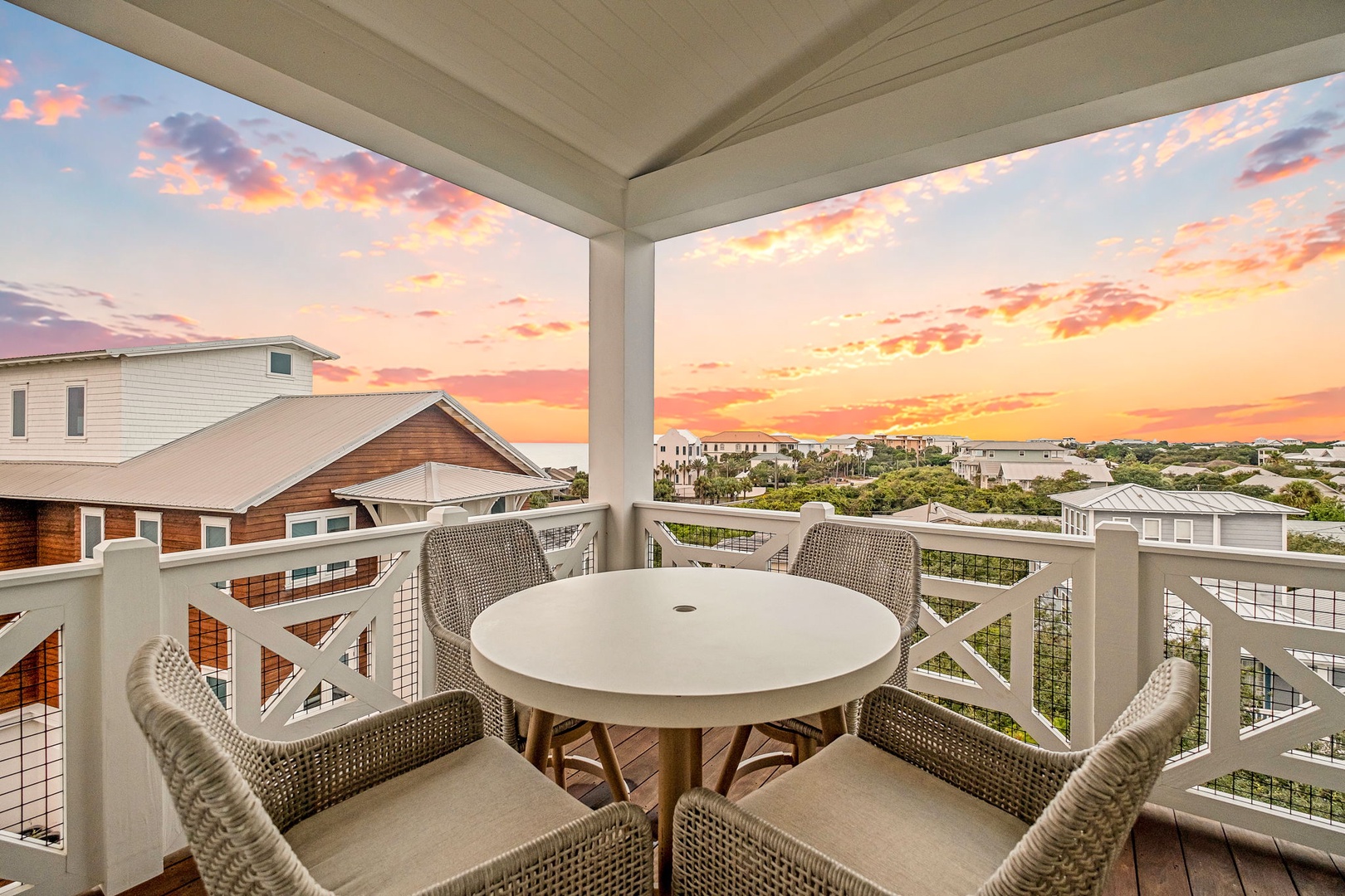 Private covered balcony featuring a dining table with comfortable seating, overlooking a scenic neighborhood with stunning sunrise or sunset views—ideal for morning coffee or evening relaxation.