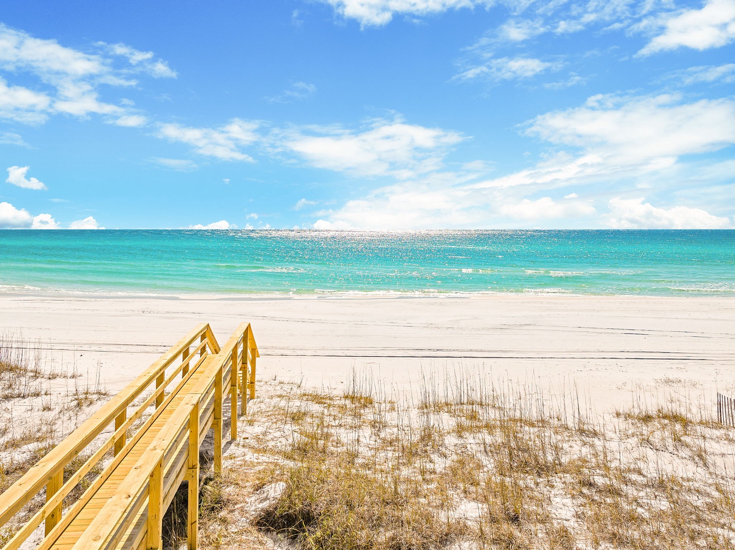Pristine white sand beach with crystal-clear turquoise waters and convenient wooden boardwalk access to the shoreline.