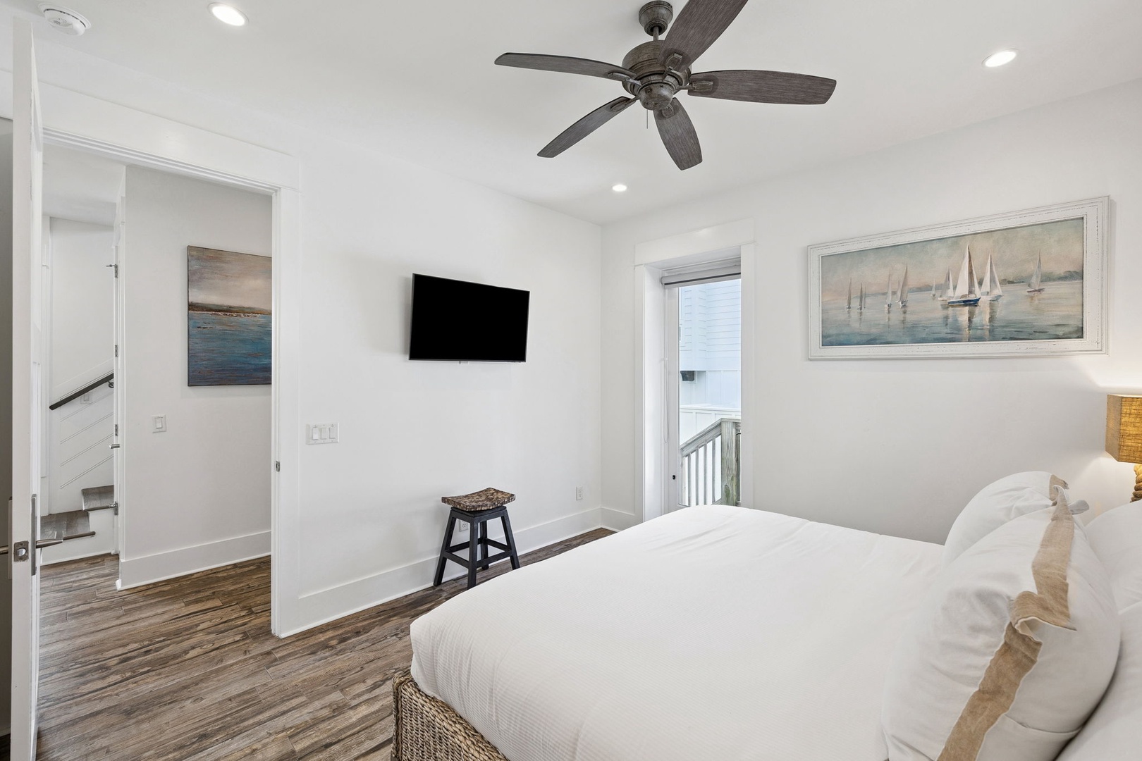 Sink into crisp white linens in your serene bedroom, where coastal artwork and a gentle ceiling fan create the perfect retreat.