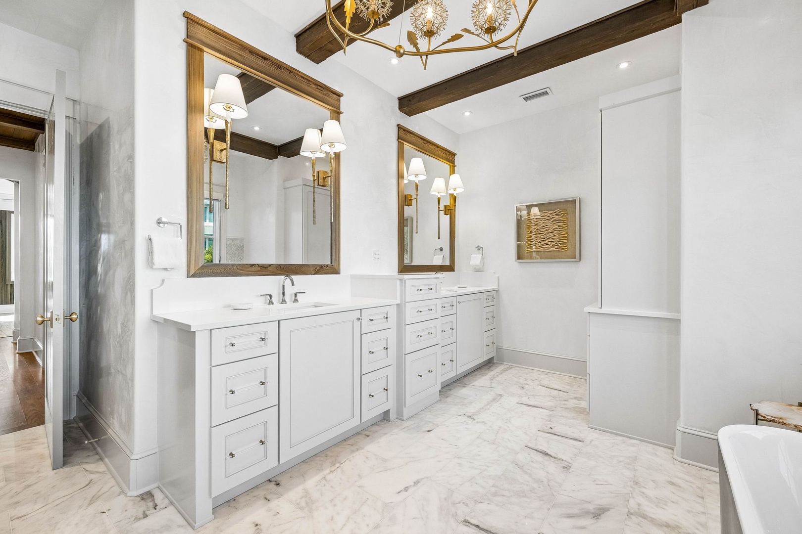 Step into your elegant ensuite bathroom, where white marble floors, dual vanities, and warm wood beam accents create a serene space to unwind after exploring the area.