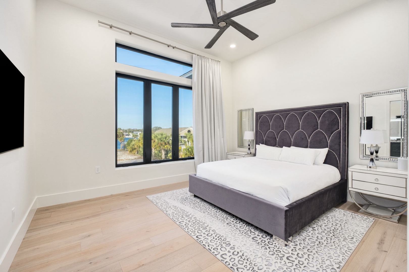 Sink into luxurious comfort in this elegant bedroom with stunning outdoor views and modern ceiling fan for your perfect night's rest.
