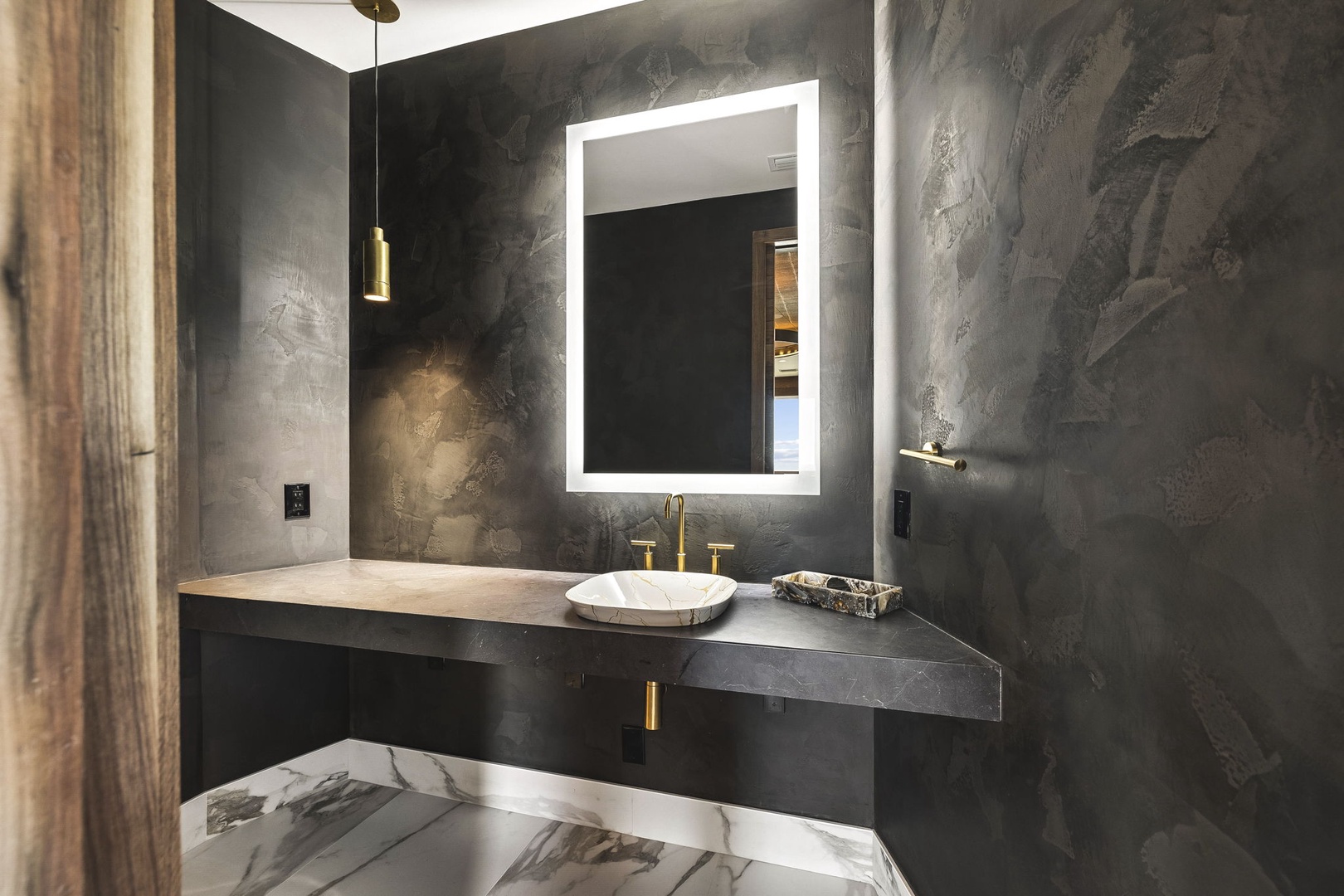 Step into your private powder room, where dramatic charcoal walls meet warm brass accents and a luminous backlit mirror—modern sophistication designed just for you.