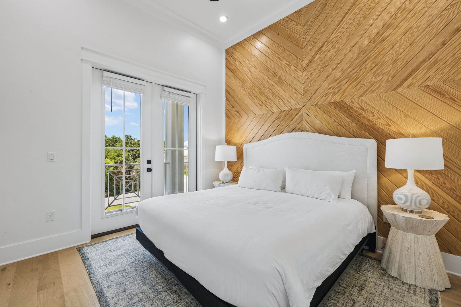 Wake to natural light streaming through glass doors that open to your private outdoor space. The striking herringbone wood accent wall and crisp white linens create a modern, serene escape.
