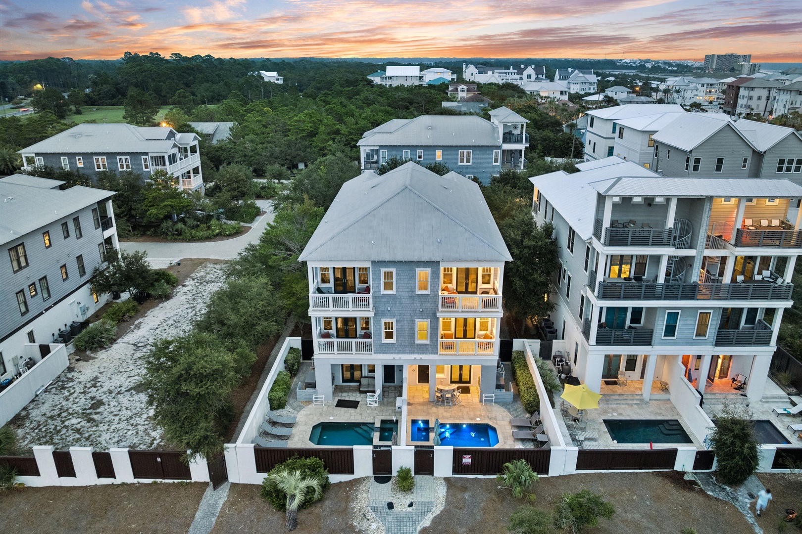 Aerial view of a coastal property nestled in a quiet residential neighborhood, featuring a private pool and surrounded by lush greenery and neighboring vacation homes.