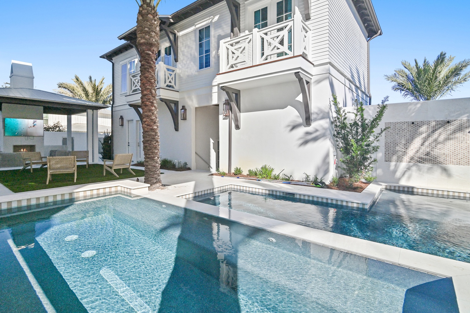 A coastal-style villa with private pool, spa feature, and covered outdoor lounge flanked by palm trees and modern landscaping.