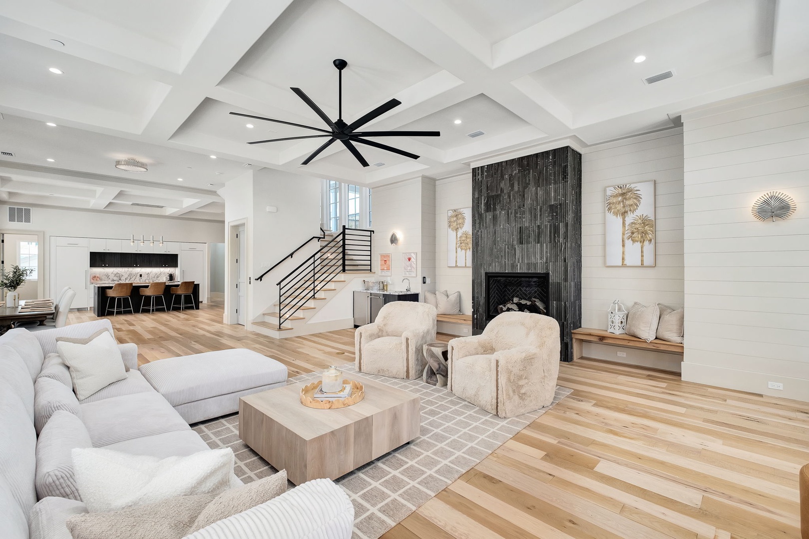 Sink into plush seating beneath soaring coffered ceilings, where warm wood floors and a striking modern fireplace create your perfect retreat.