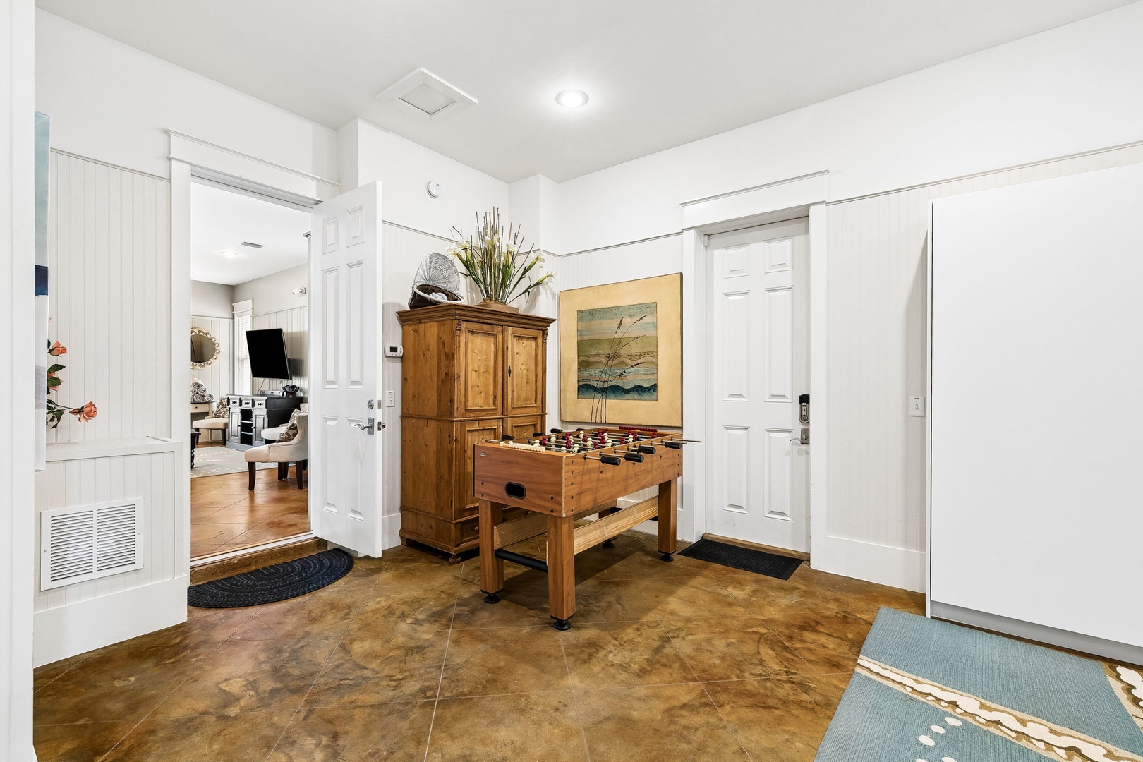 Step through the welcoming entry into your vacation home, where a foosball table and charming wooden armoire set the tone for relaxed coastal living. Multiple doorways lead to shared spaces designed for your comfort and fun.