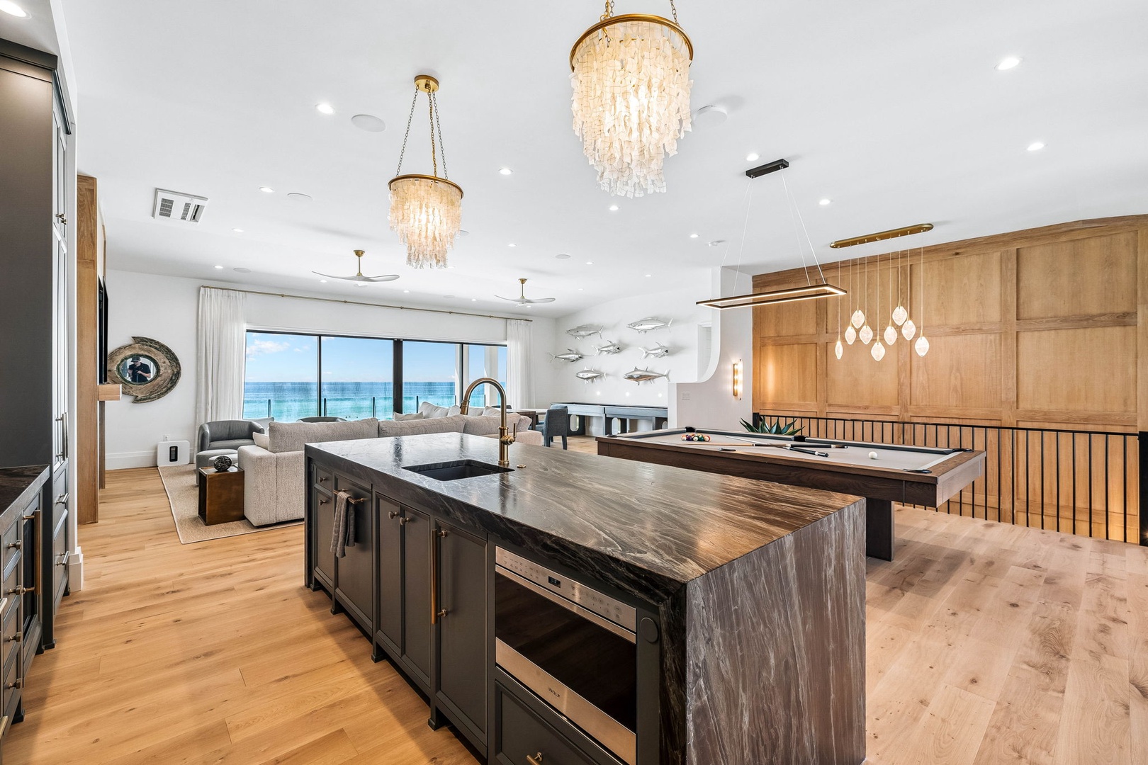 Stunning ocean views frame your dream vacation space, where warm wood tones and elegant chandeliers create a luxurious beachside retreat you'll never want to leave.