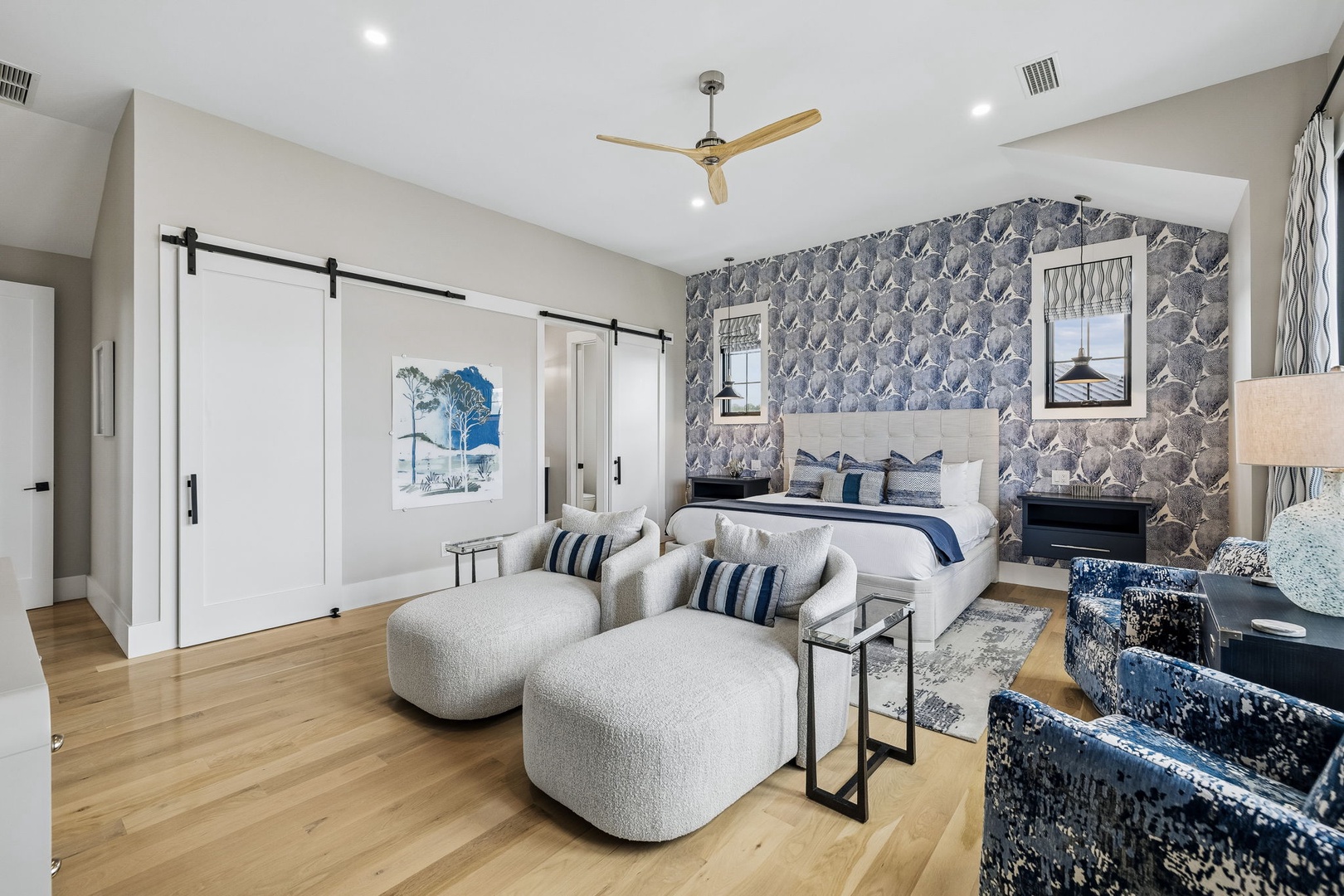 Sink into plush seating and unwind in your beautifully appointed bedroom, where coastal elegance meets modern comfort. The stylish barn doors and soothing blue-gray palette create a peaceful retreat perfect for relaxation.