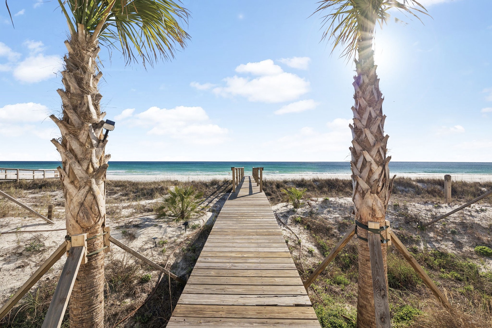 A wooden boardwalk leads through coastal dunes to pristine white sand beaches and turquoise waters.