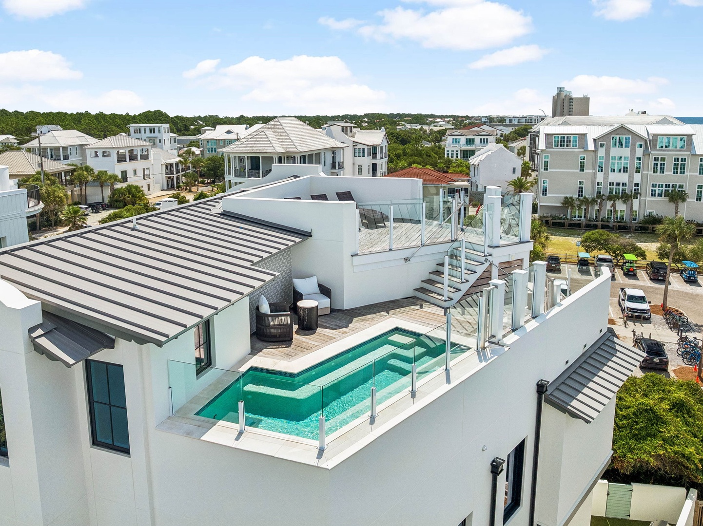 Aerial view of a modern luxury vacation rental featuring a private rooftop pool, terrace seating, and multiple levels in a coastal residential neighborhood with contemporary architecture.
