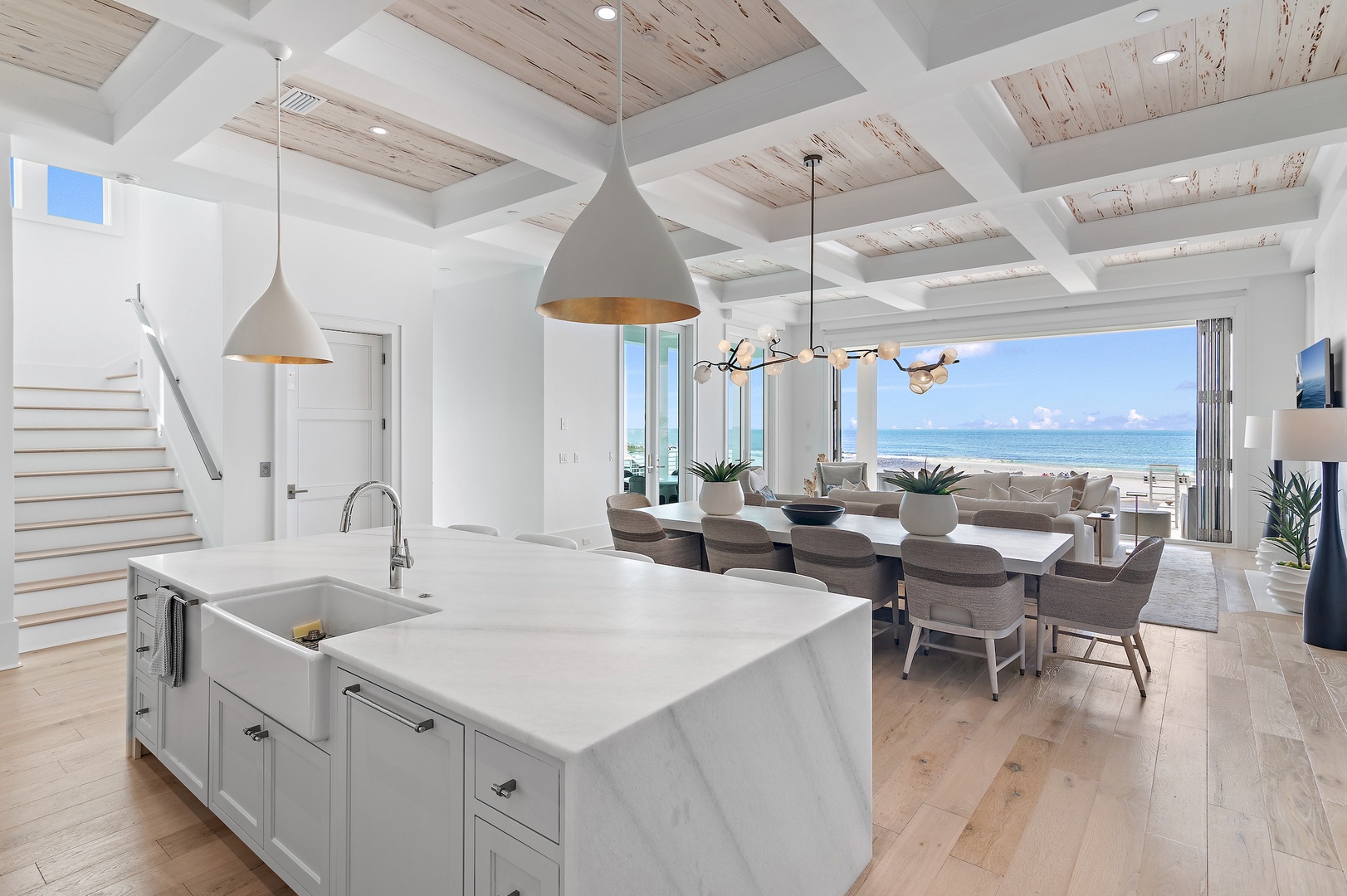 Coastal sanctuary with soaring coffered ceilings and floor-to-ceiling windows framing endless ocean views. Open kitchen flows into dining and living spaces perfect for gathering, with the sea sparkling just beyond your door.