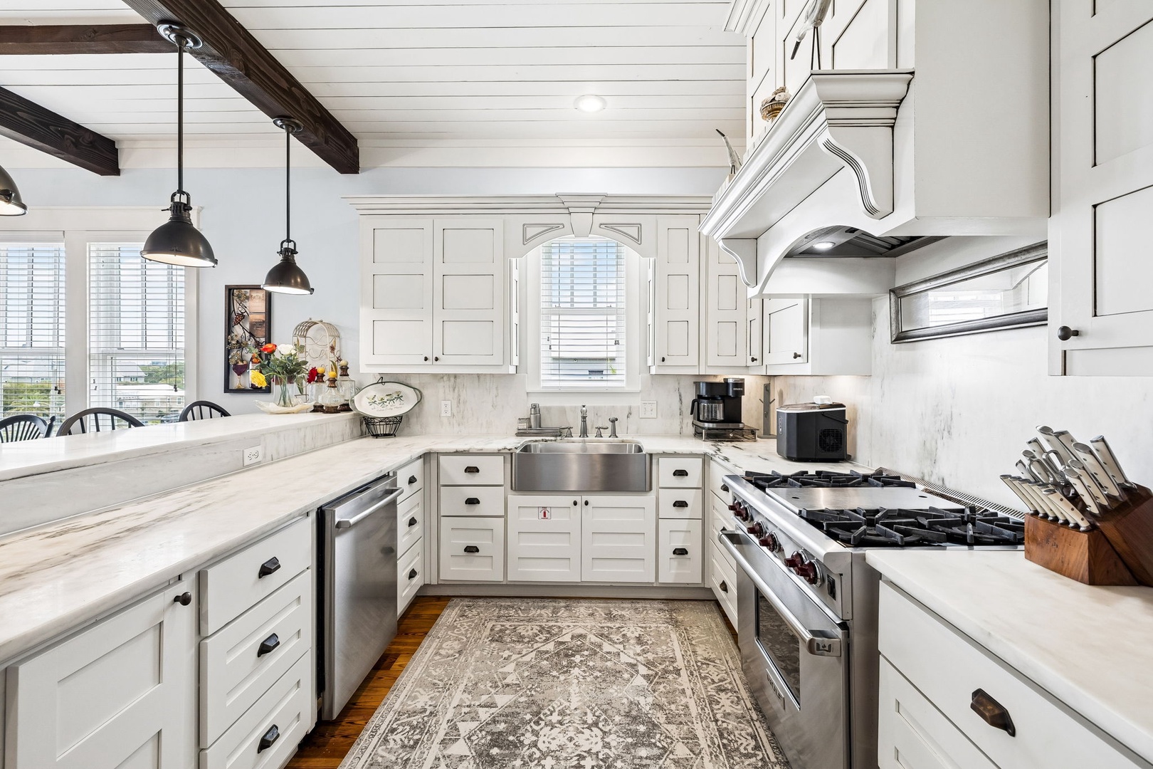 Step into your gourmet kitchen with gleaming marble counters, a professional-grade gas range, and charming pendant lights overhead. Exposed beams and elegant cabinetry create a warm, inviting space for cooking and gathering.