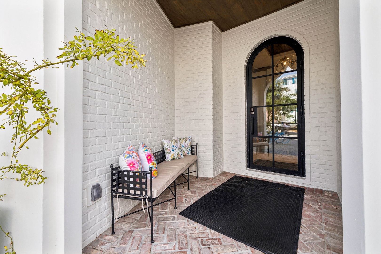 A welcoming covered entryway with patterned brick flooring and a charming bench for you to pause before stepping through the elegant arched door.
