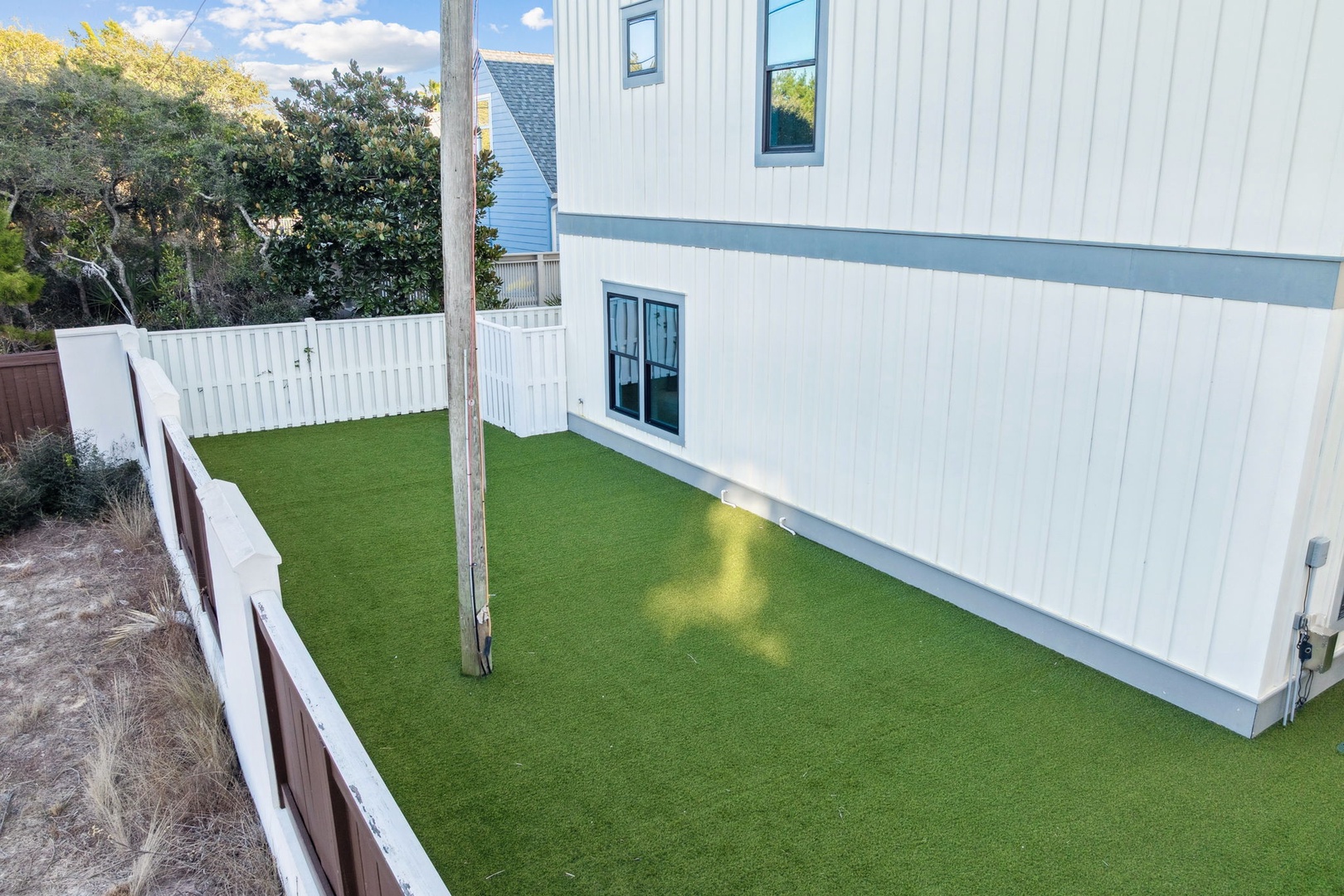 Step onto your private artificial turf patio where sunshine creates perfect patterns on the pristine green surface, surrounded by peaceful fencing.