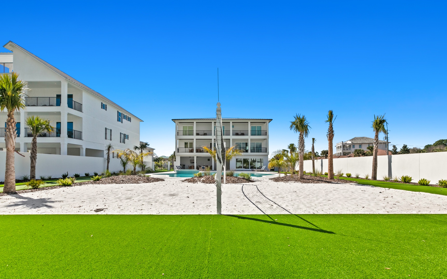 A pristine beachfront property with tropical landscaping and a sparkling pool awaits your coastal getaway. The lush lawn and palm trees frame your modern retreat beneath the bright blue sky.