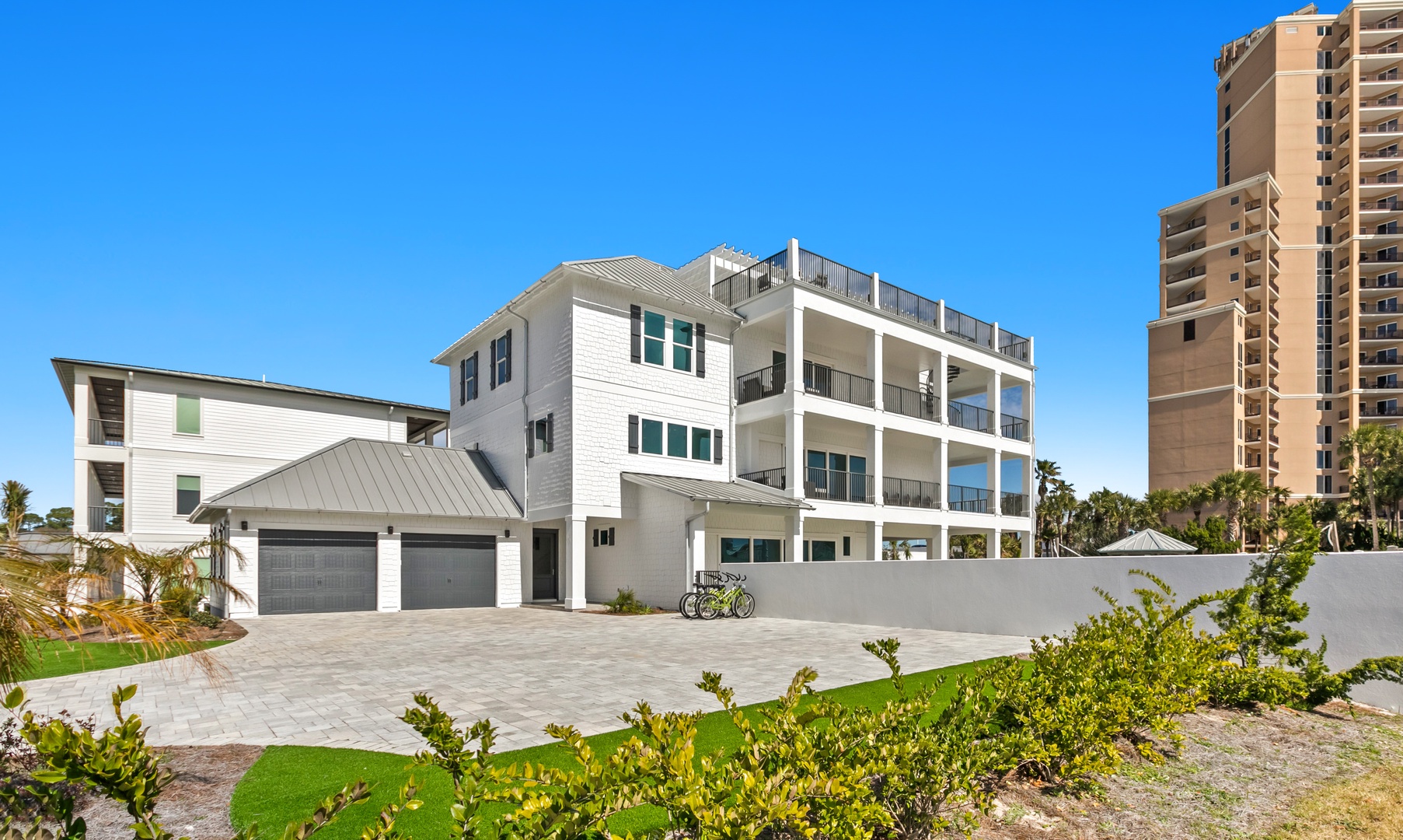 A modern coastal property featuring spacious balconies and multiple levels, offering a beachside retreat surrounded by palm trees and nearby high-rise buildings.