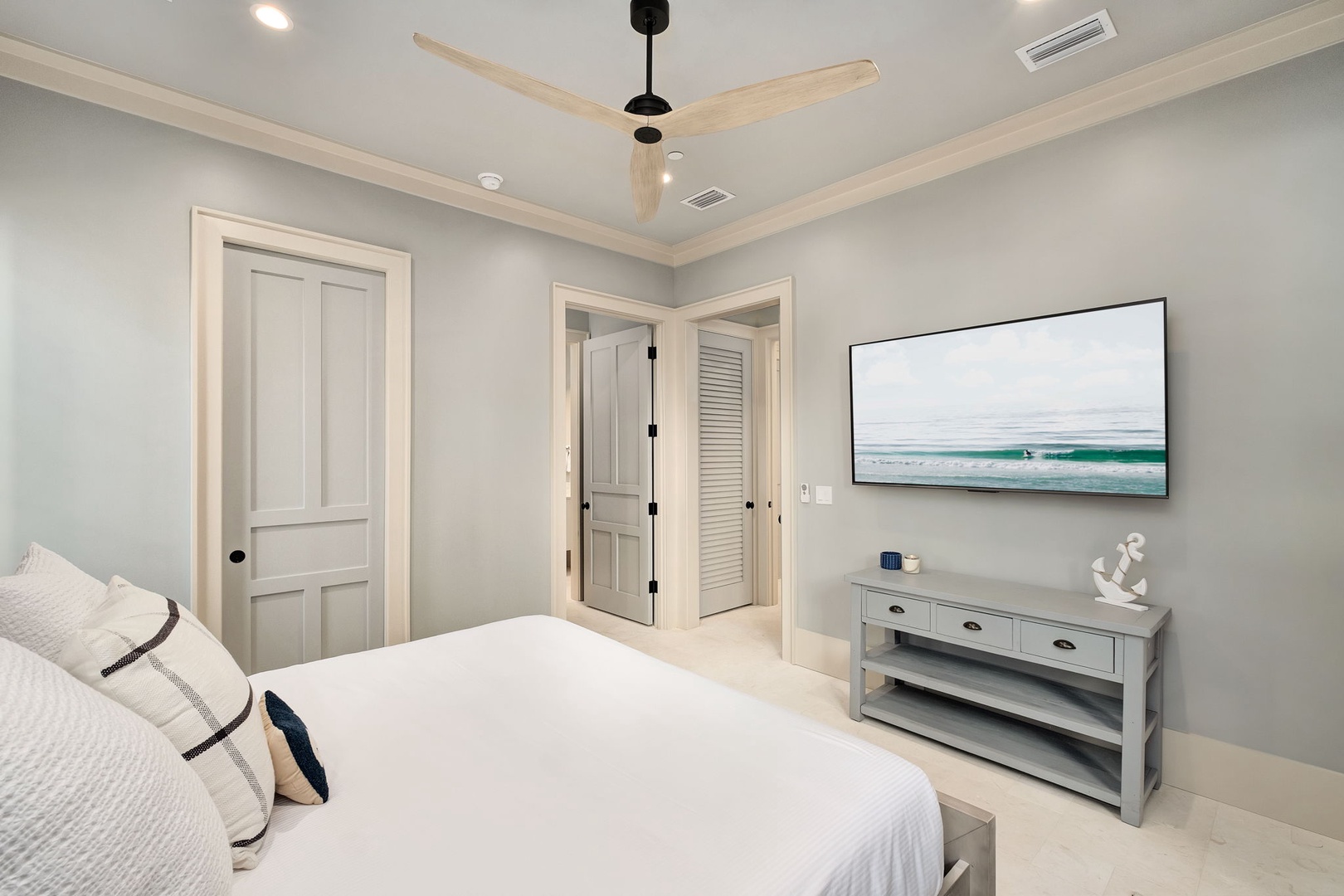 Drift off to peaceful slumber in your serene bedroom, featuring coastal charm and modern comfort beneath gentle ceiling fan breezes.