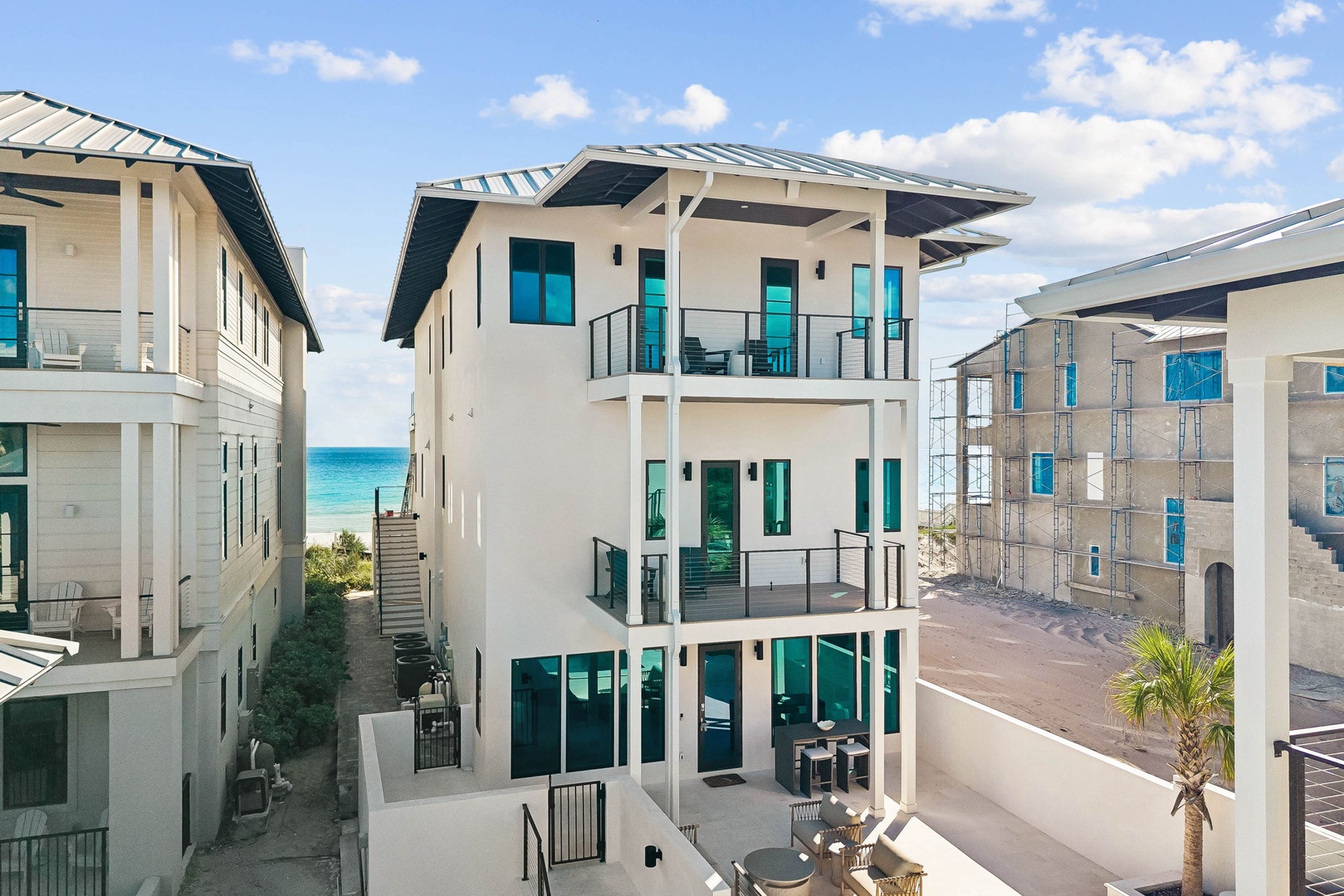 This modern three-story beachfront property showcases contemporary architecture with multiple balconies overlooking turquoise gulf waters, situated in a coastal neighborhood with direct beach access.